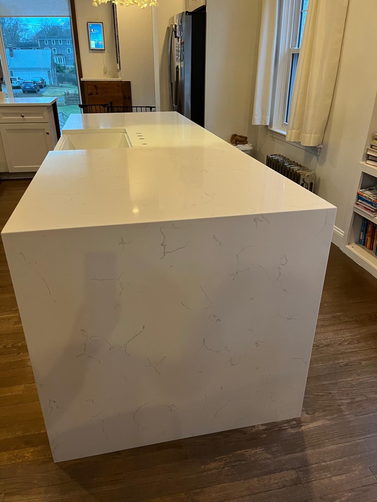 White kitchen island with a cooktop, hardwood floor, and a window in the background.