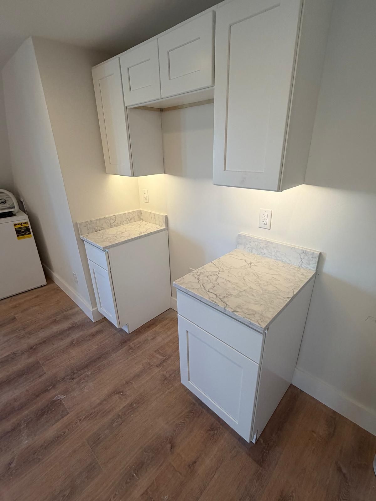White kitchen cabinets with light countertops and under-cabinet lighting.
