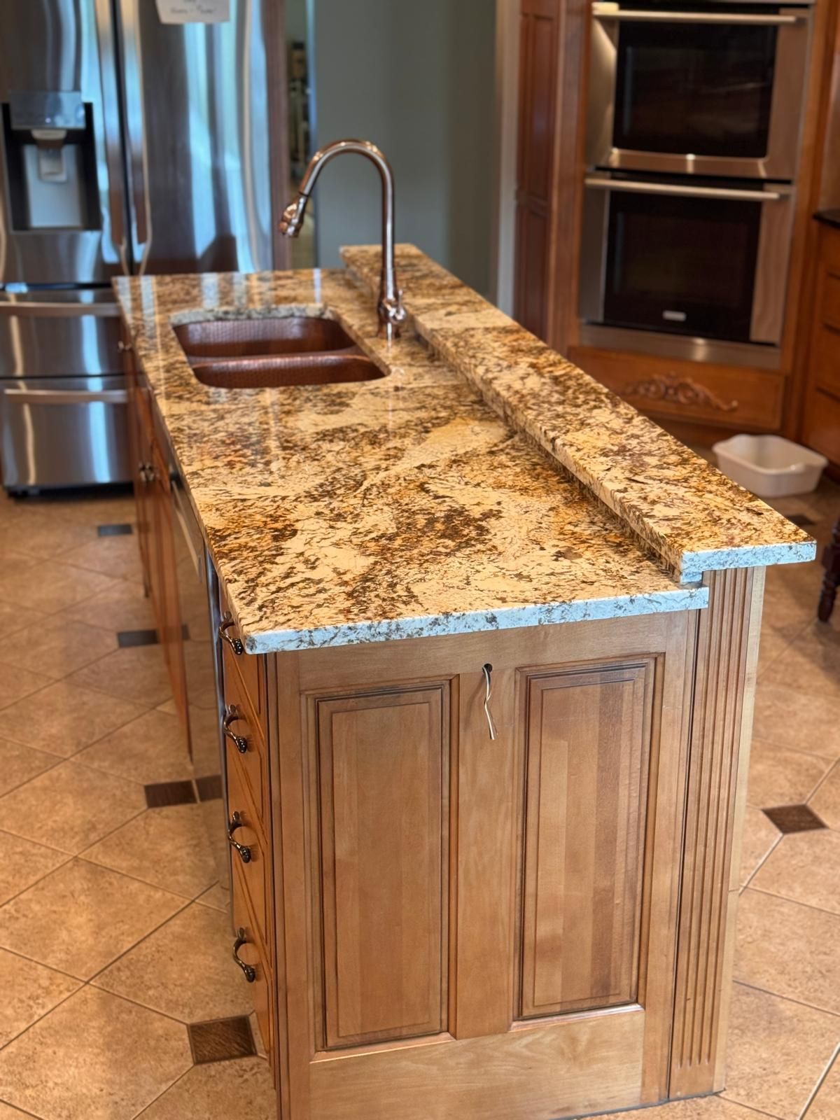 Kitchen island with granite countertop, copper sink, and stainless steel faucet, with wooden cabinets.