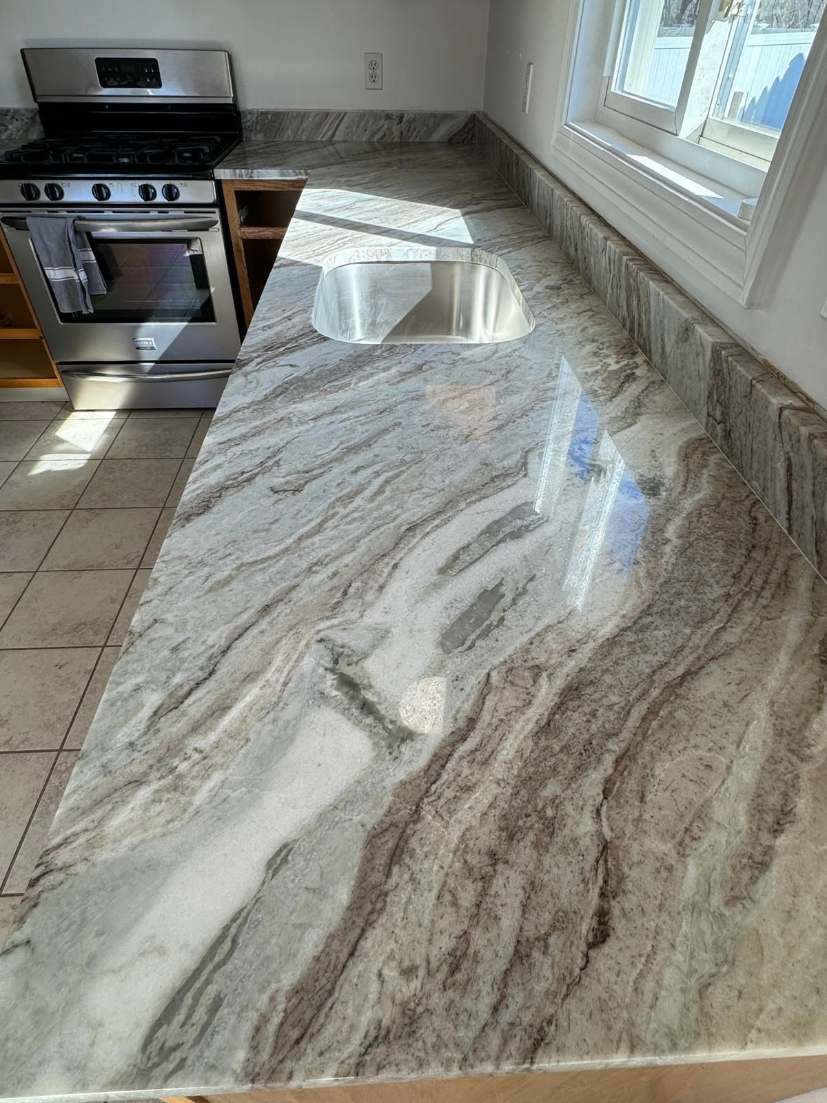 Granite countertop with sink, near window and stove. Swirling gray and white patterns.