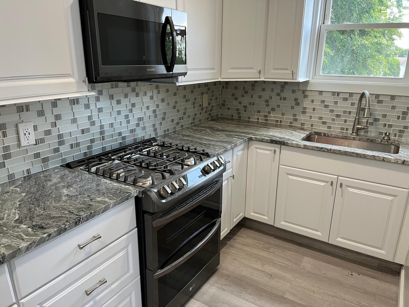 A modern kitchen with white cabinets, gray countertops, and a gas stove.