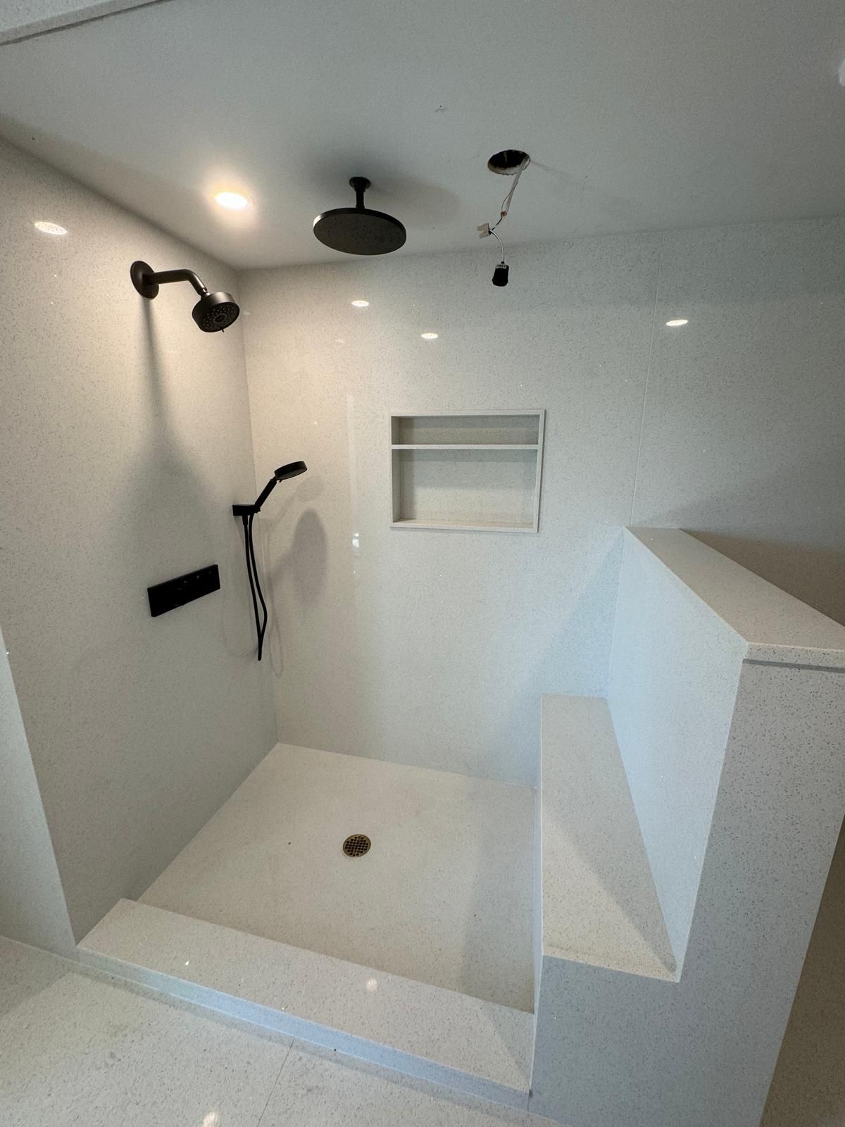Modern bathroom shower with white speckled tile, black shower fixtures, and a built-in bench.