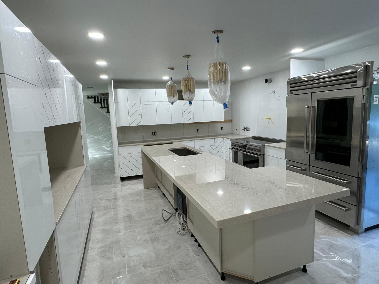 Modern white kitchen with island, stainless steel appliances, and pendant lights.