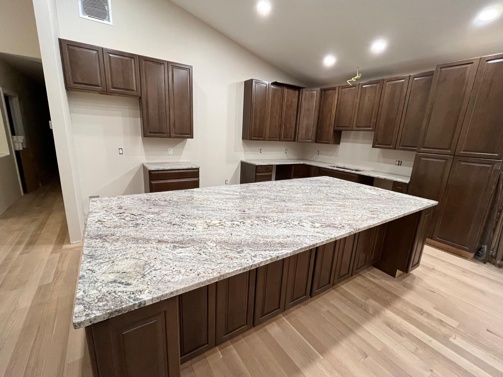 Kitchen with brown cabinets, granite countertops, and light wood floors.