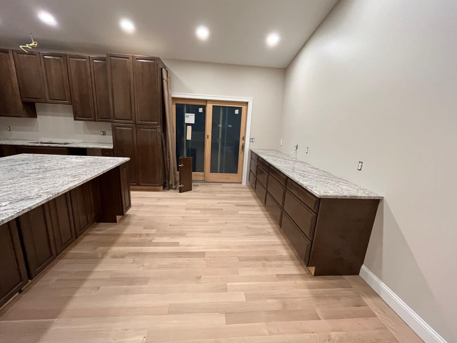 Kitchen with dark brown cabinets, light countertops, and light wood floors. Sliding glass door in the background.