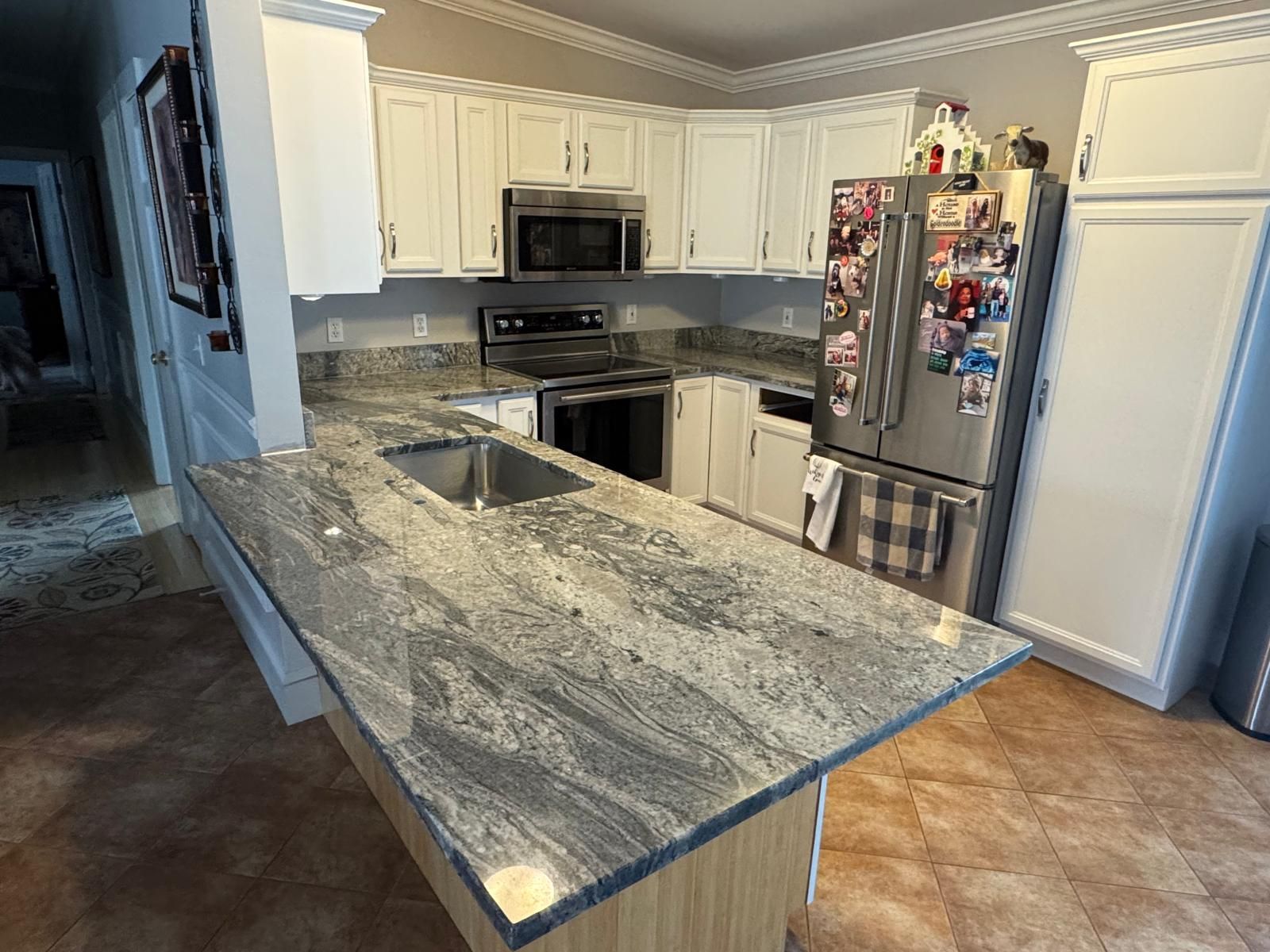 Kitchen with granite countertops, white cabinets, stainless steel appliances, and a central island.
