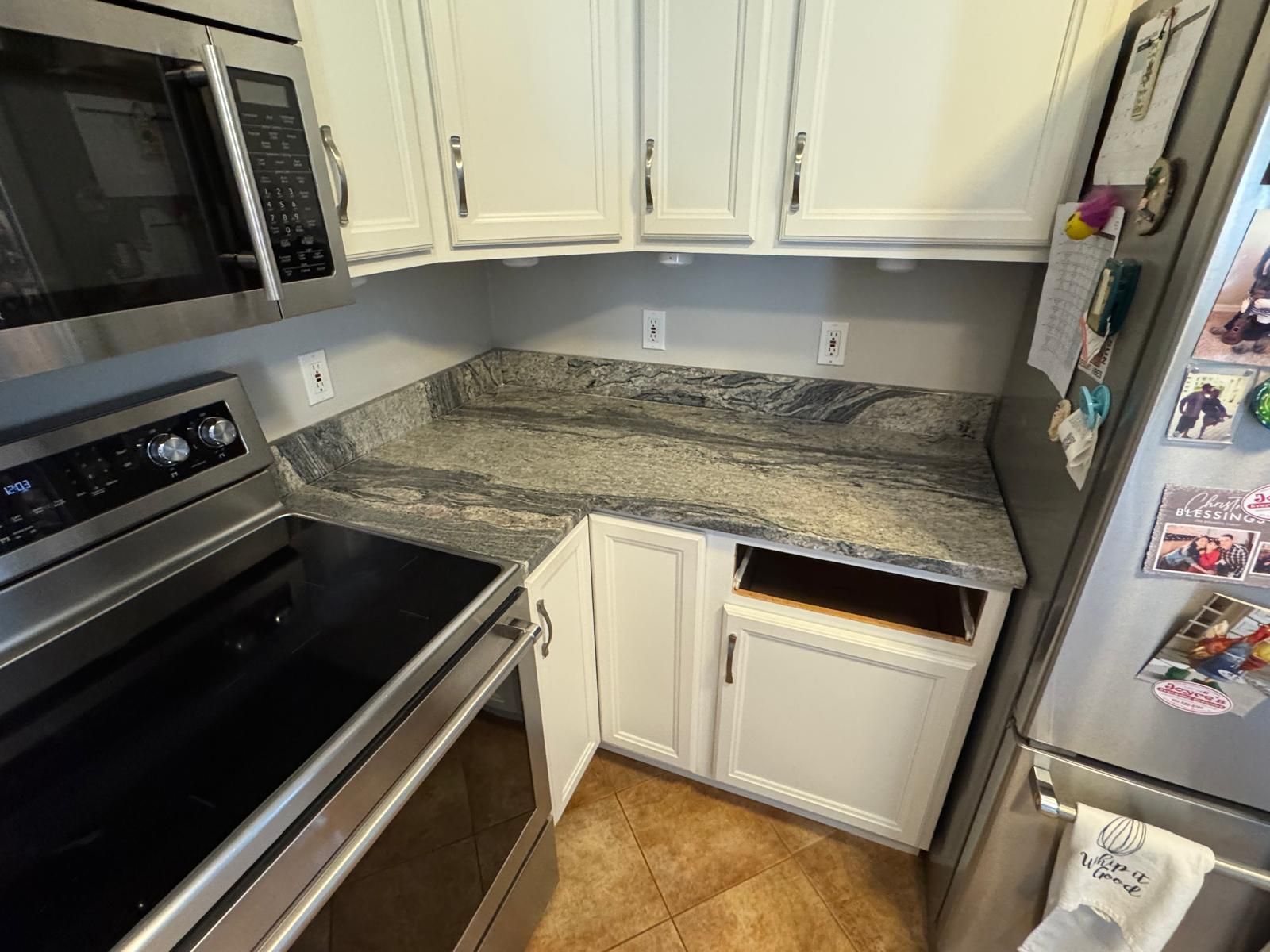 Kitchen corner with white cabinets, gray countertops, and a stainless steel oven and microwave.