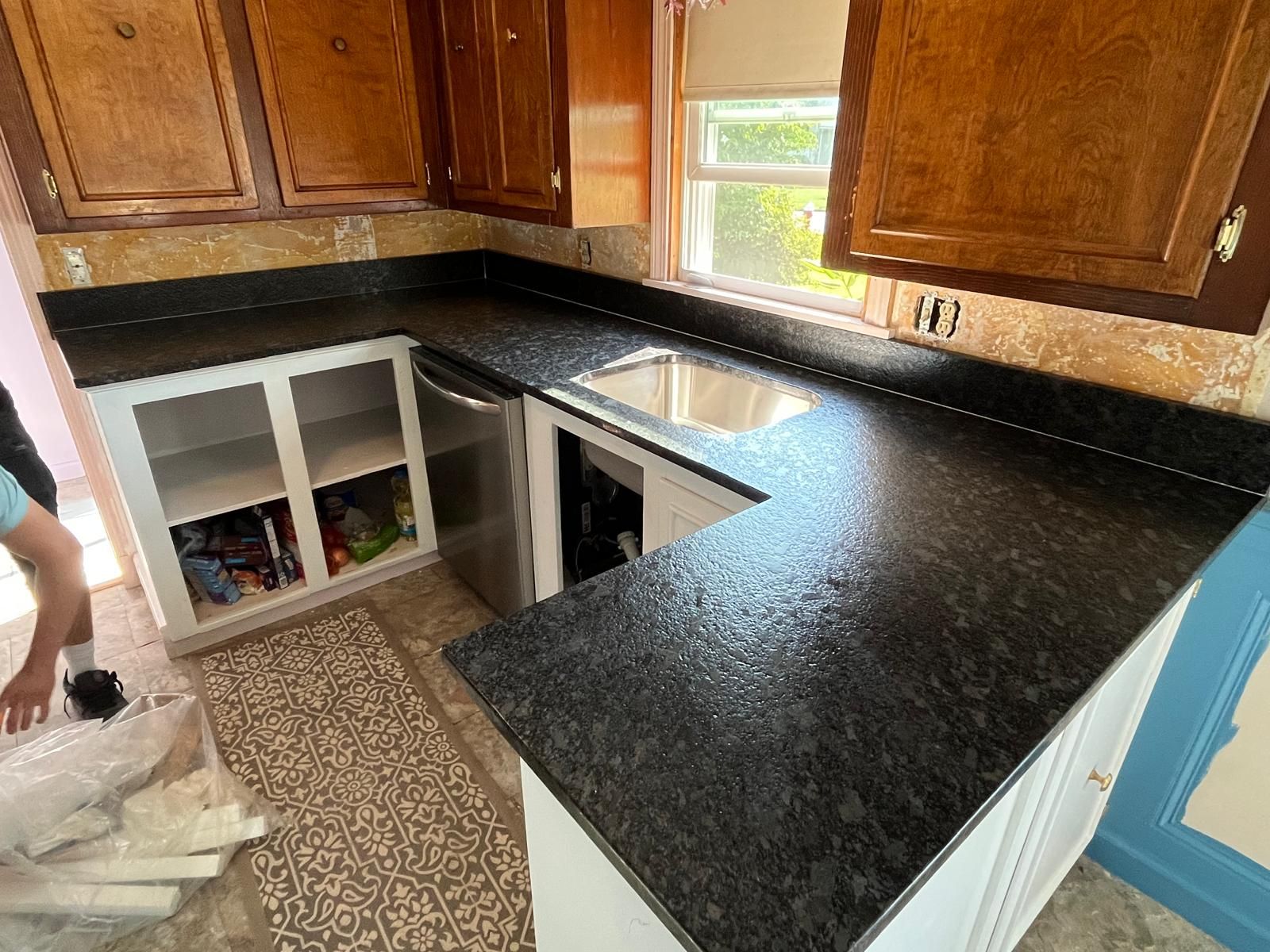 Kitchen with dark countertop, white cabinets, stainless steel sink, and wood cabinets.