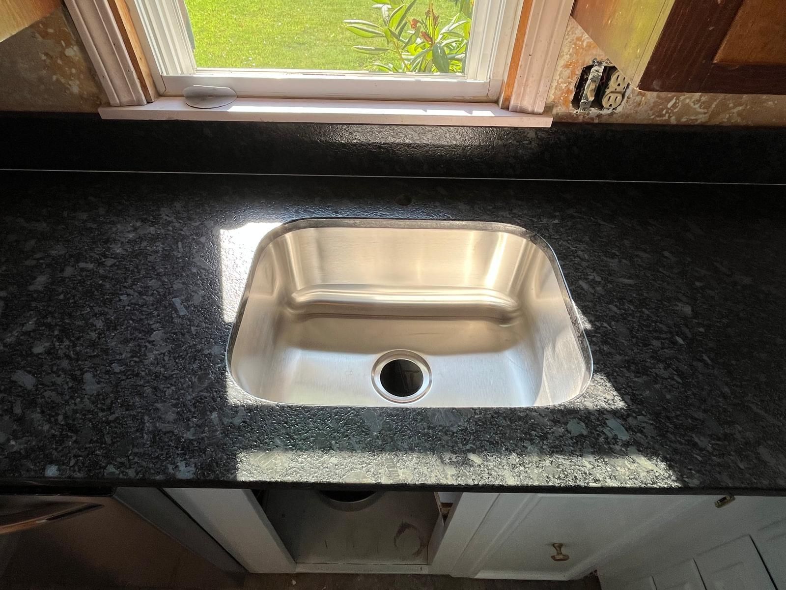 Stainless steel kitchen sink in a dark granite countertop, under a window.