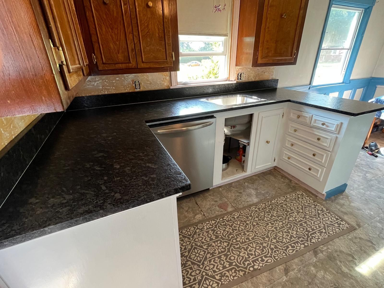 A kitchen with dark countertops, white cabinets, and a stainless steel dishwasher.