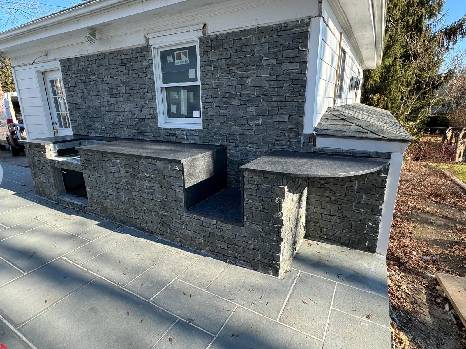Building exterior with dark stone veneer, flat-top tables, and a concrete patio.