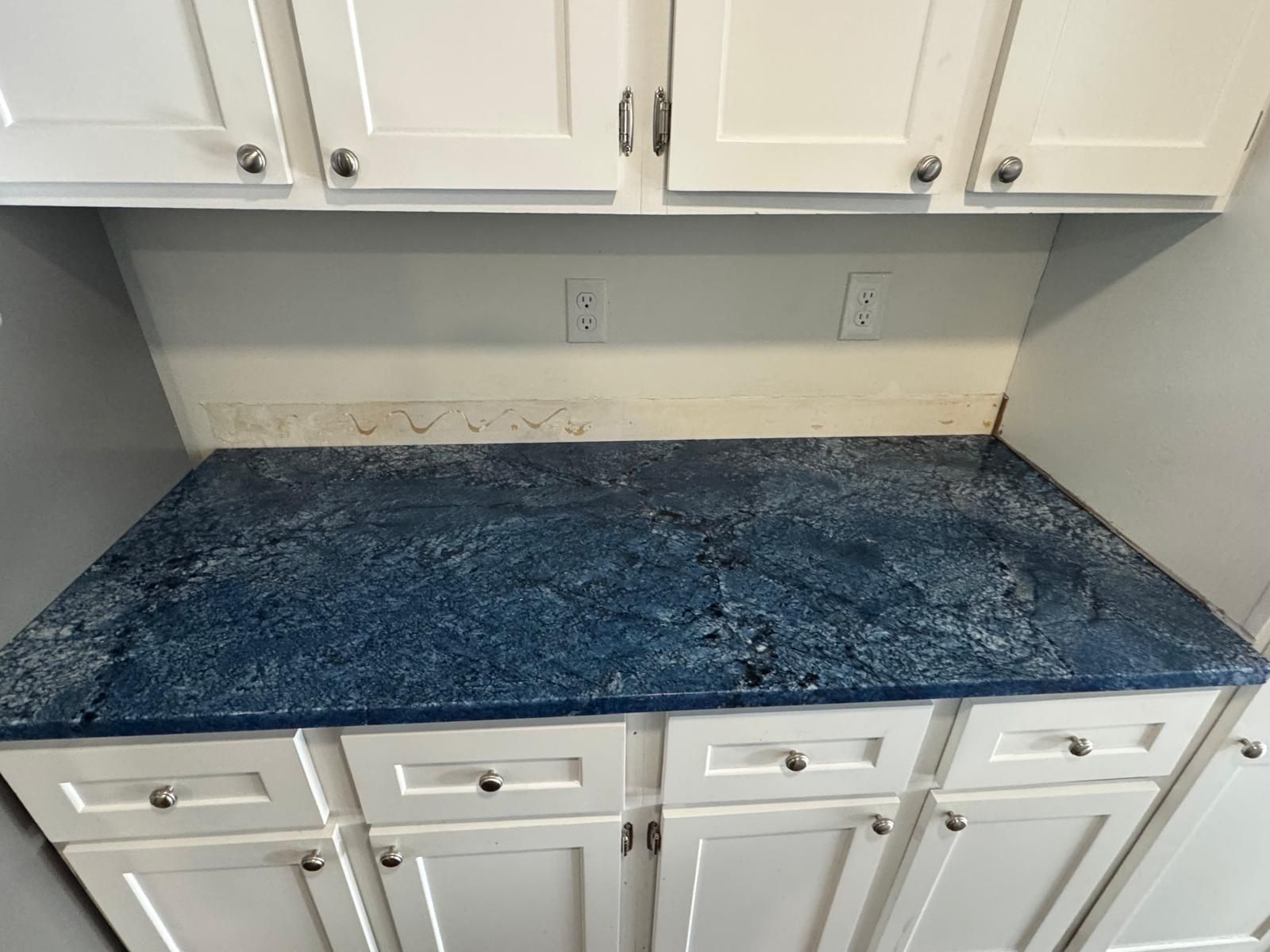 Blue countertop with dust, under white cabinets, with upper cabinets above.