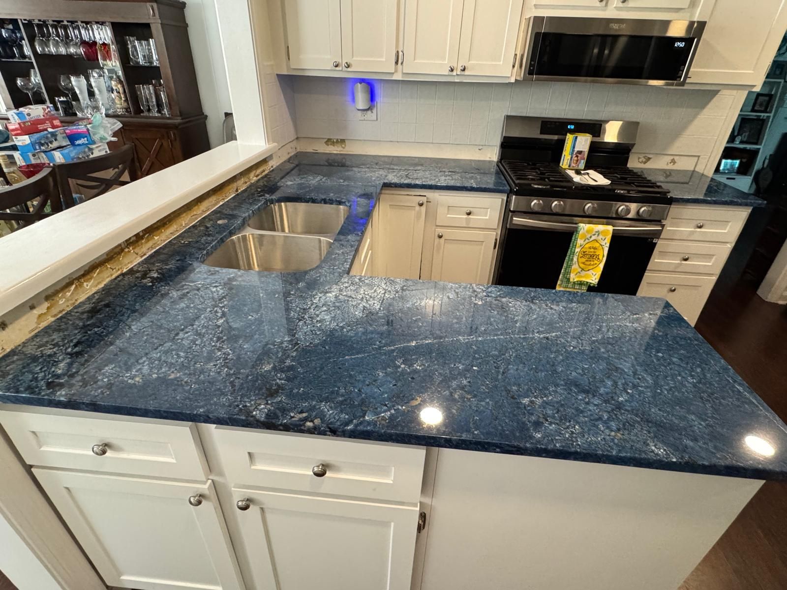 Blue speckled kitchen countertop with white cabinets, stainless steel sink, and stove.