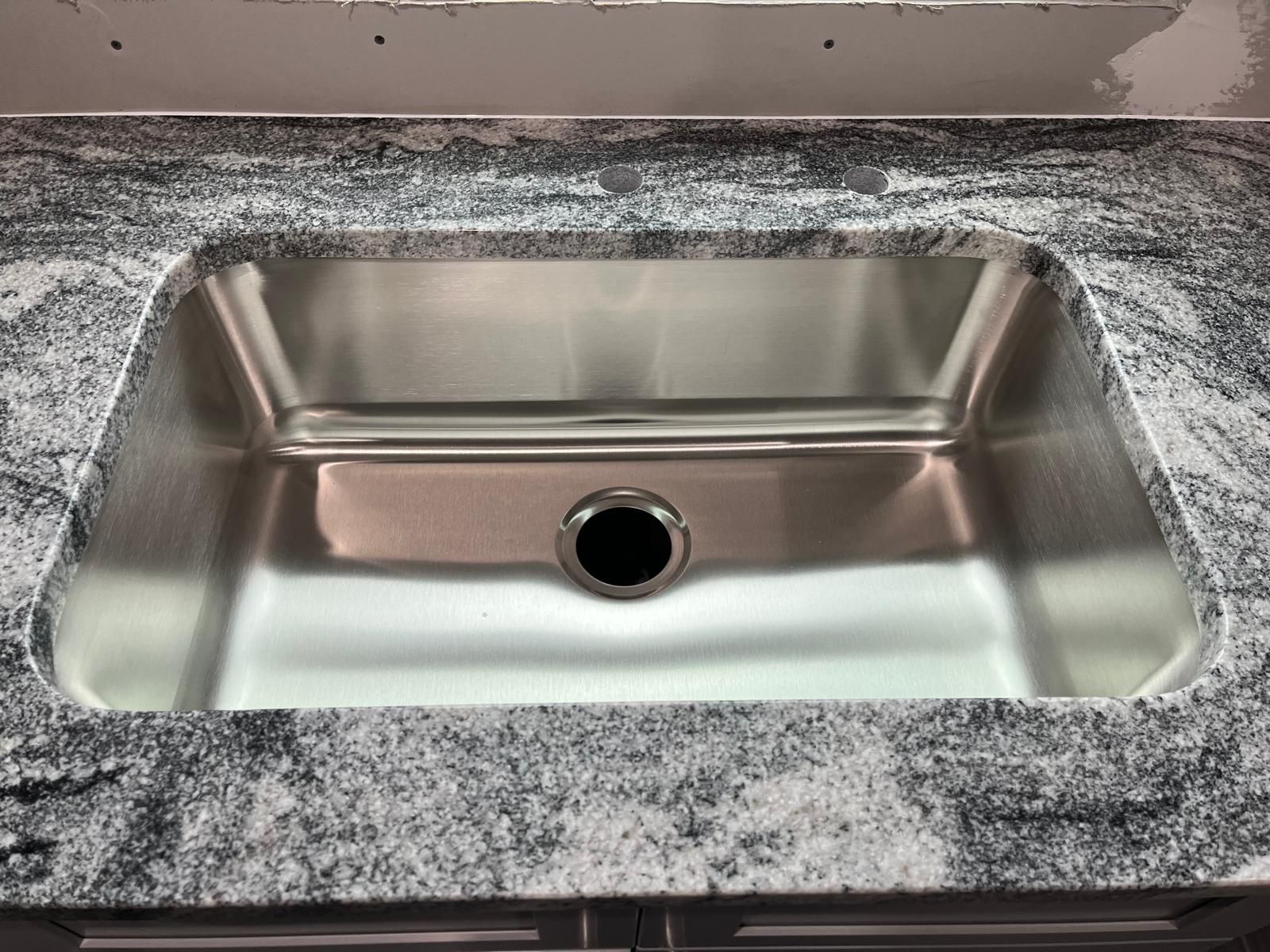 Stainless steel kitchen sink installed in gray granite countertop.