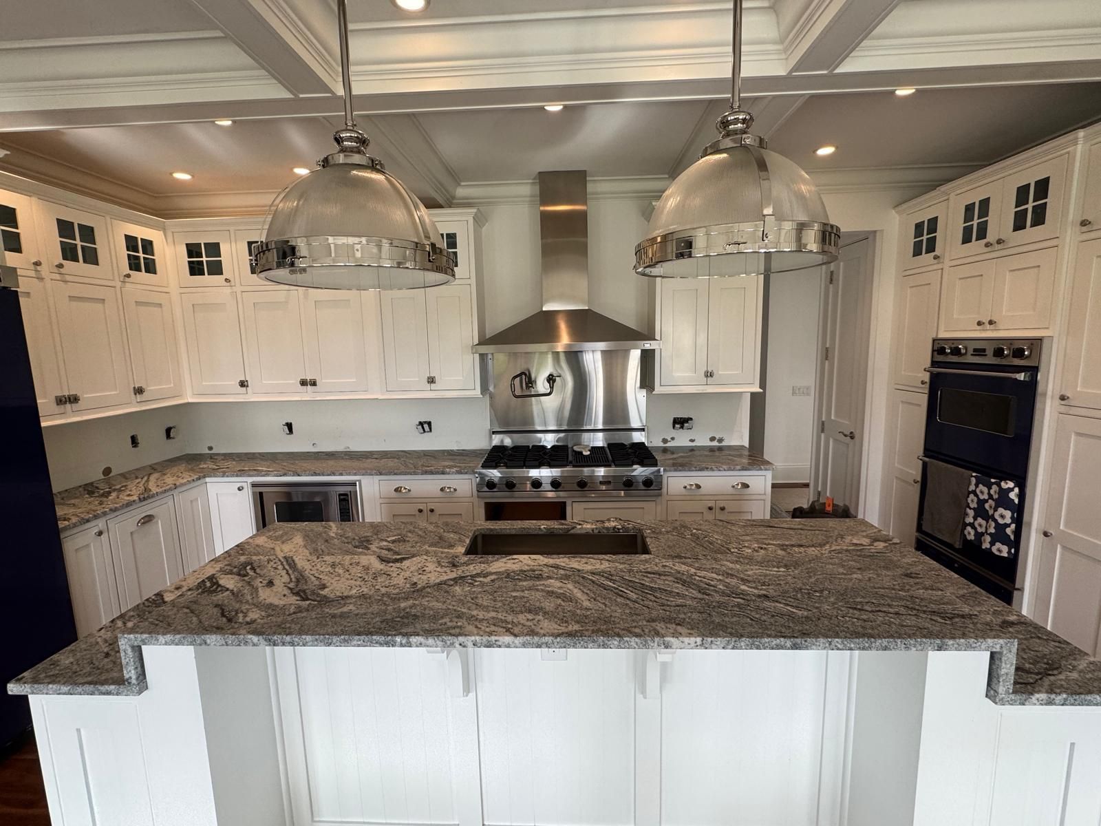 White kitchen with granite countertops, stainless steel appliances, and pendant lights.