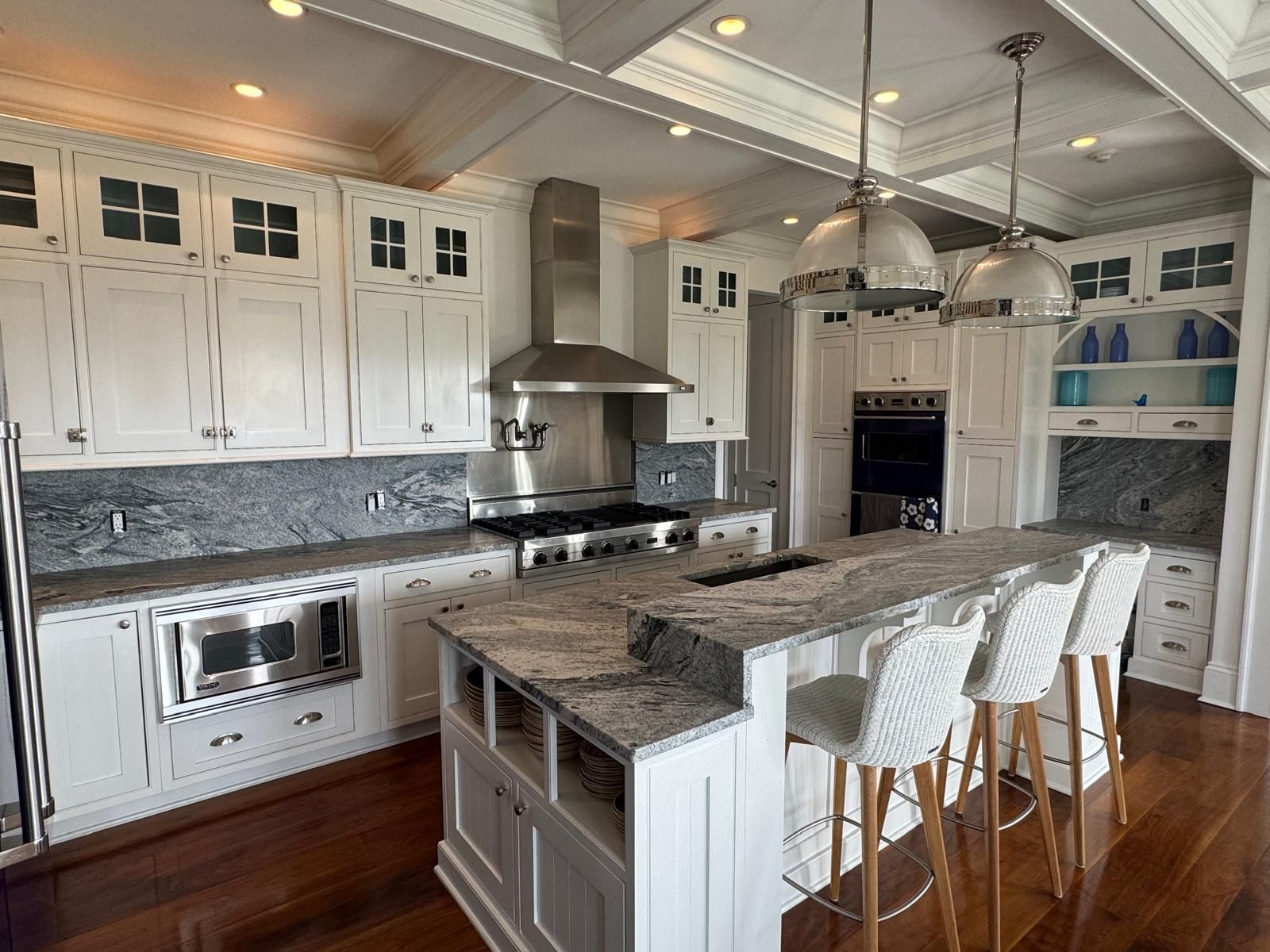 White kitchen with stainless steel appliances, granite countertops, and a central island with bar stools.