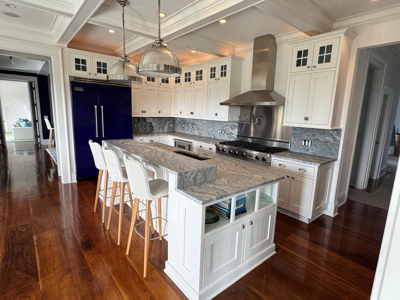 White kitchen with blue fridge, island with seating, and stainless steel range hood.