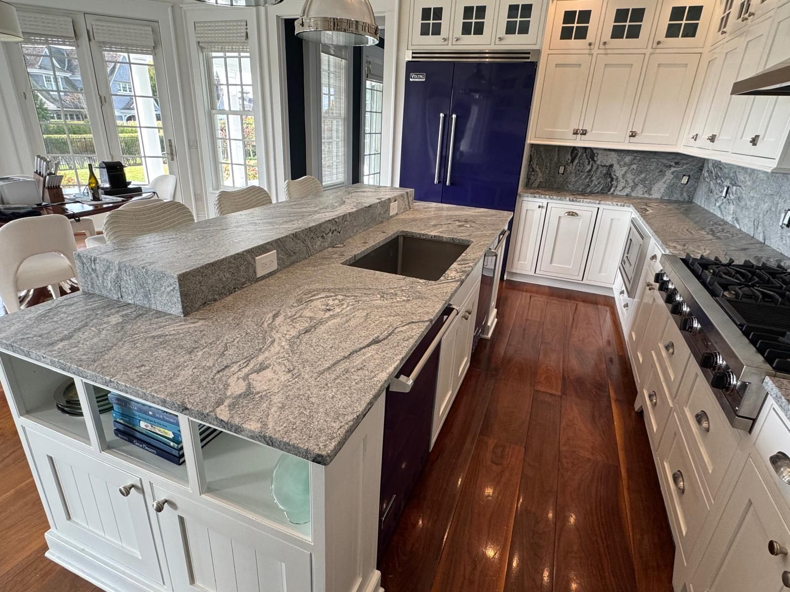 Kitchen with white cabinets, gray countertops, blue fridge, and wooden floors.