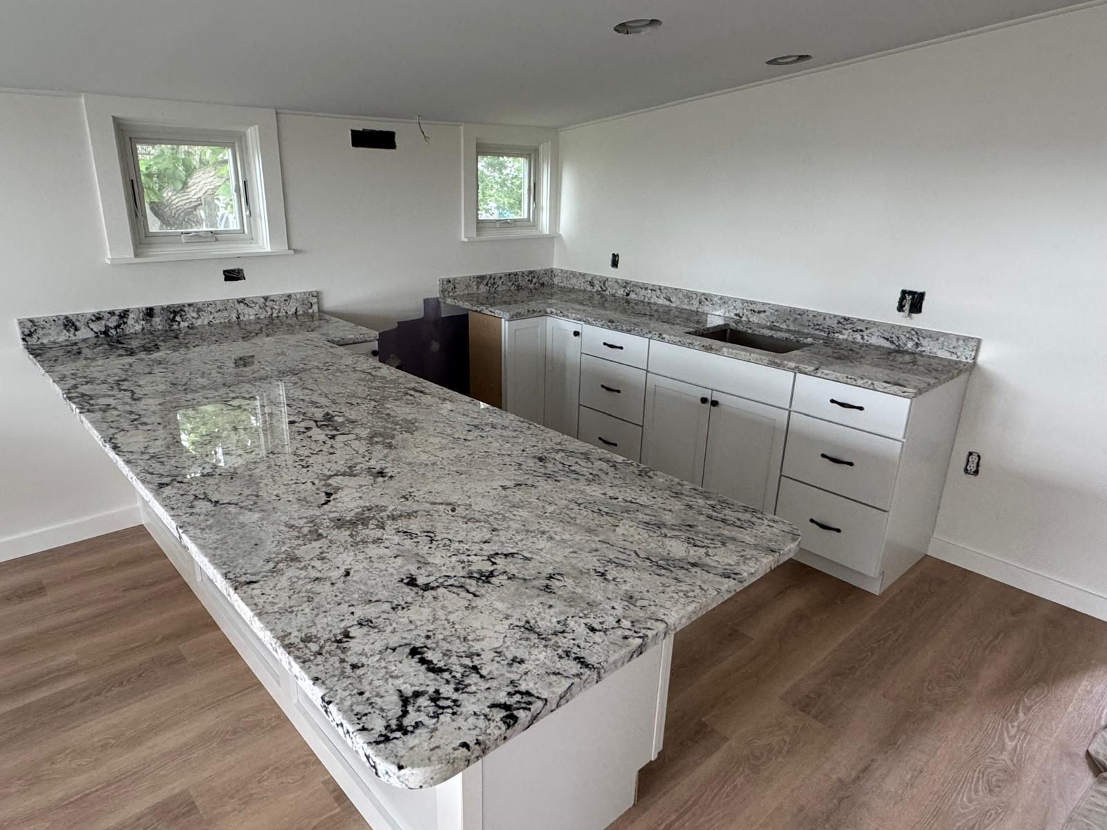 Kitchen with white cabinets, granite countertops, and light wood flooring.