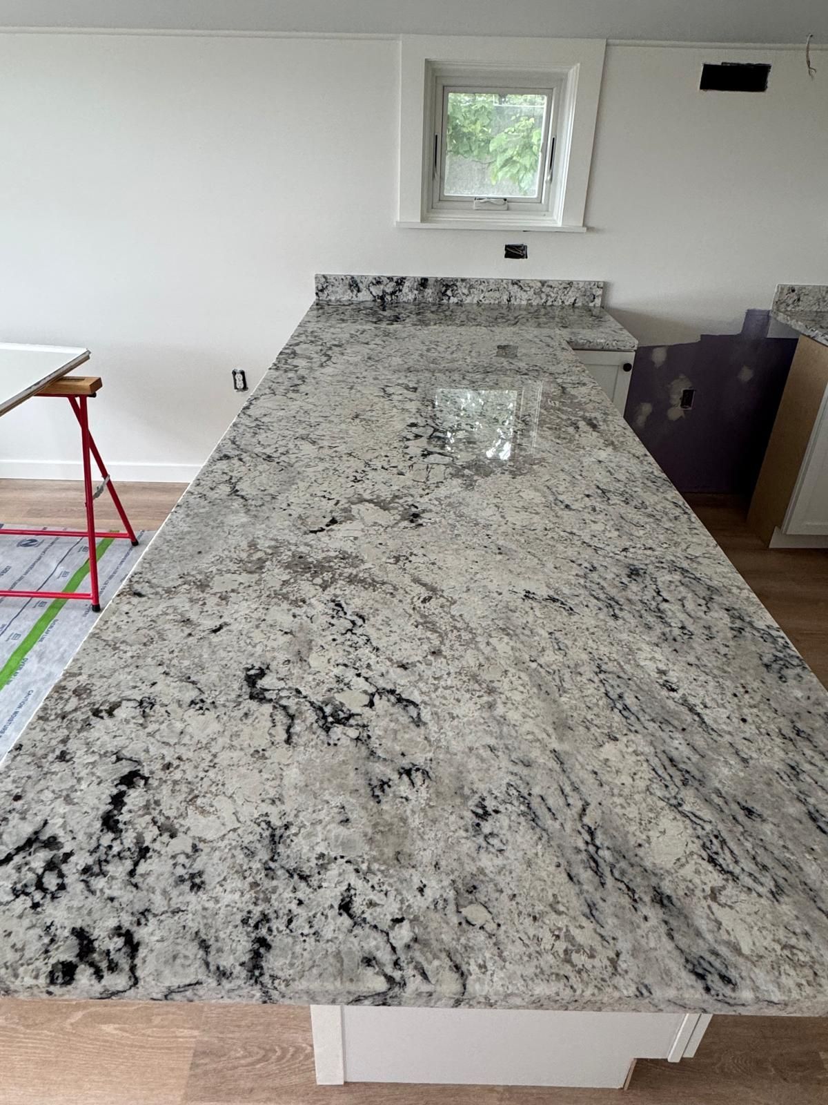 Granite countertop in a kitchen with a small window and a white cabinet base.