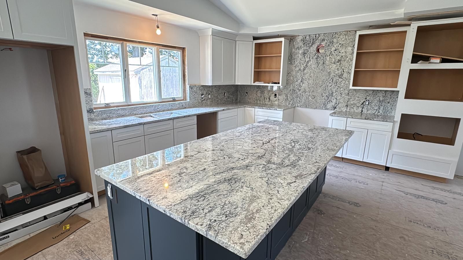 Kitchen under construction, with white cabinets, granite countertops, and a gray island.