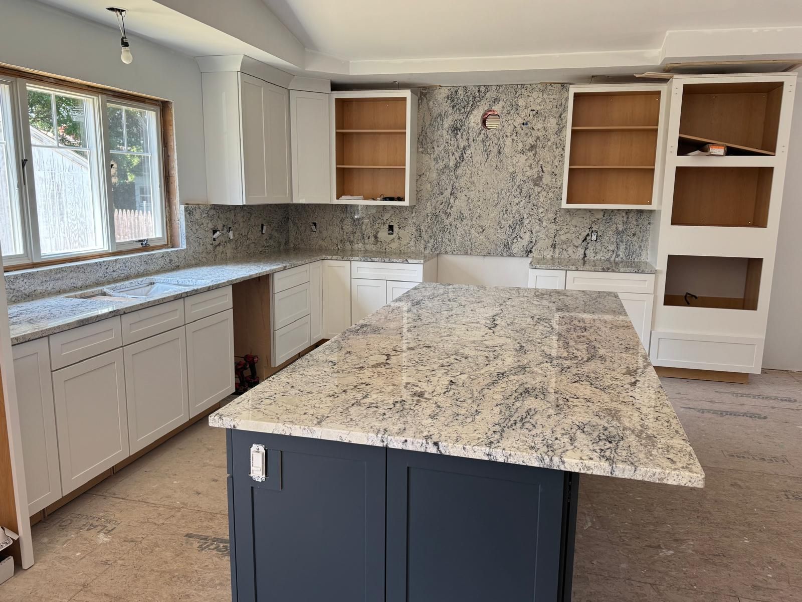 Kitchen under construction with granite countertops, white cabinets, and a blue island.