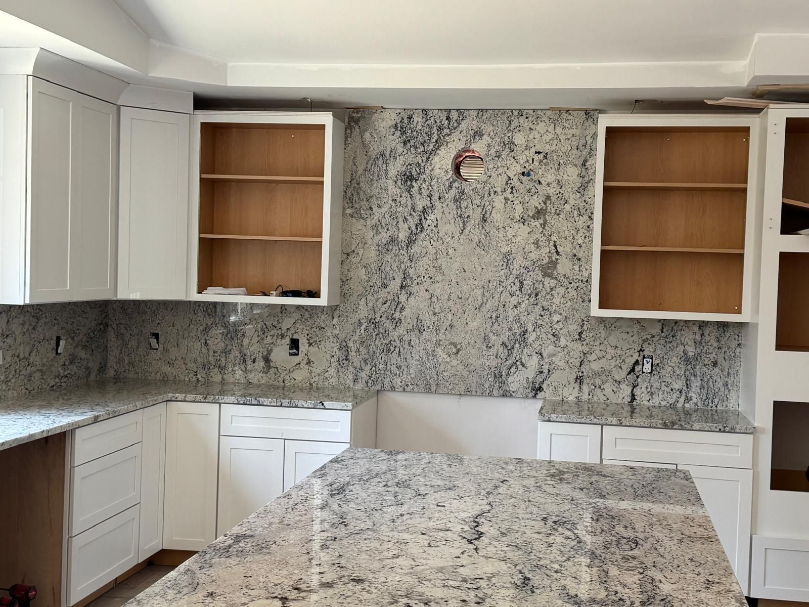 Kitchen under construction with white cabinets, granite countertops, and exposed wall.