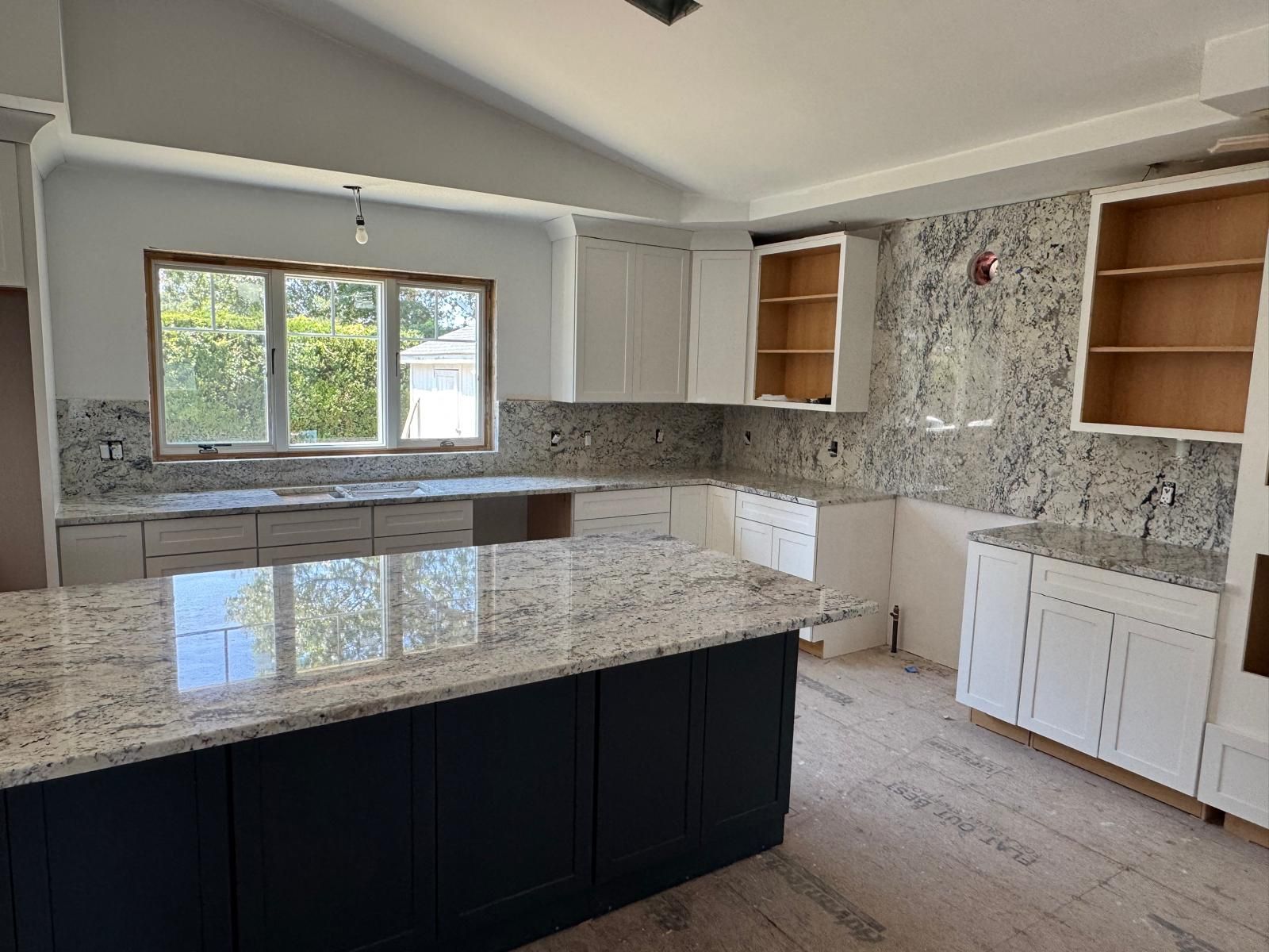 Newly renovated kitchen with white cabinets, granite countertops, and a dark blue island.