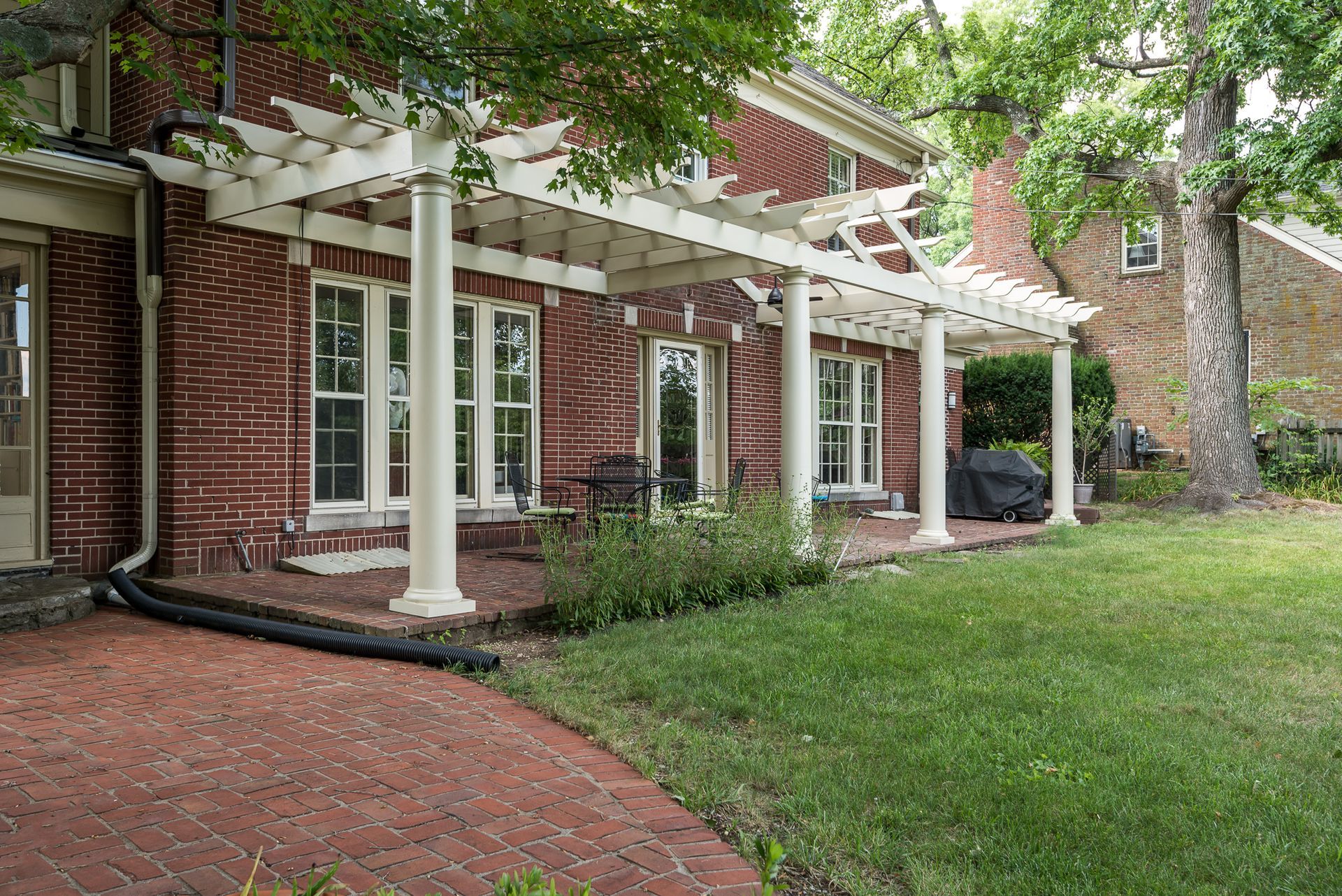 A brick house with a white pergola on the front porch.