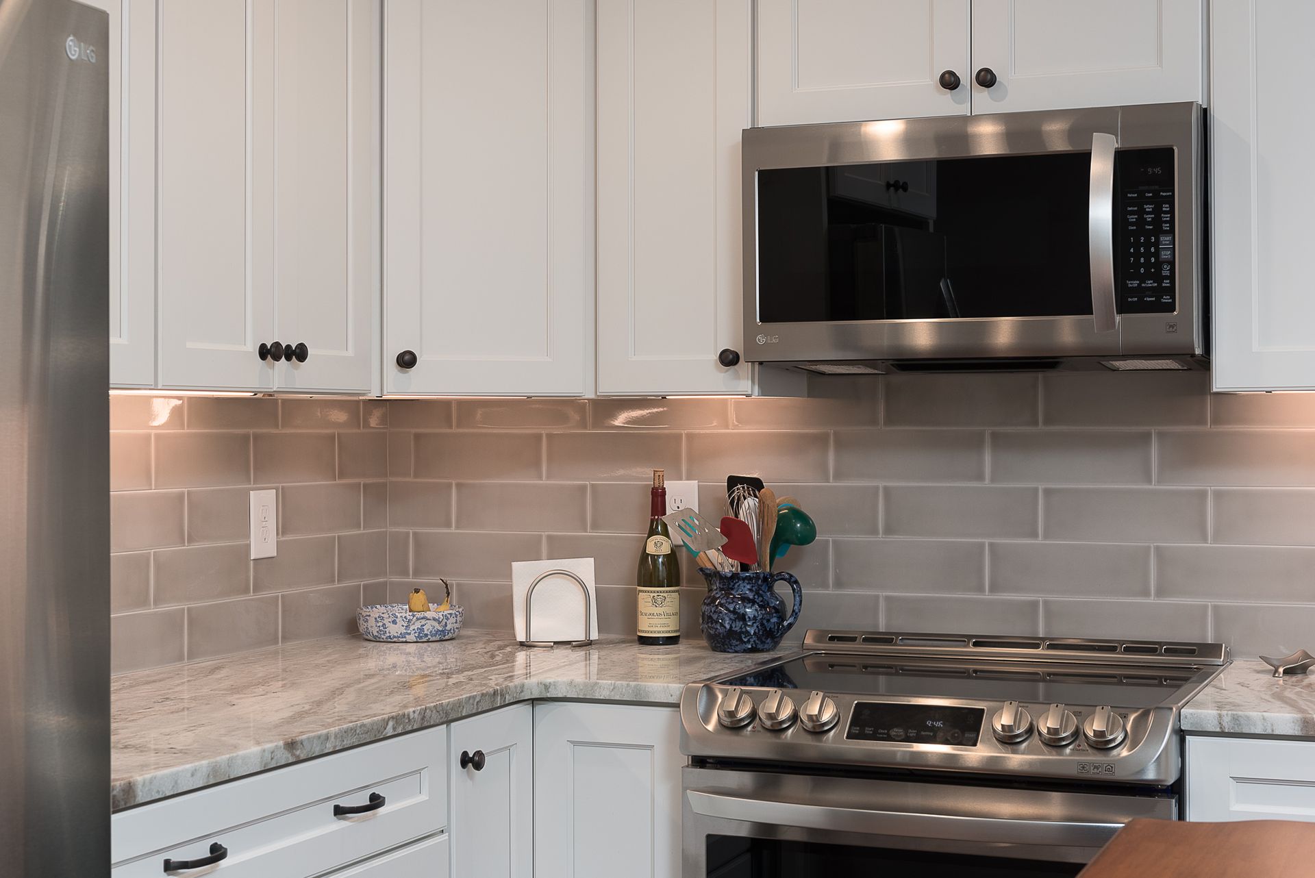 A kitchen with white cabinets , a stove , a microwave , and a refrigerator.