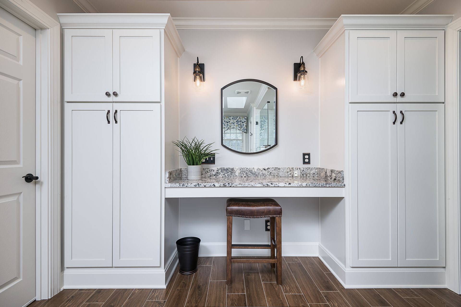A bathroom with white cabinets , a vanity , a mirror and a stool.