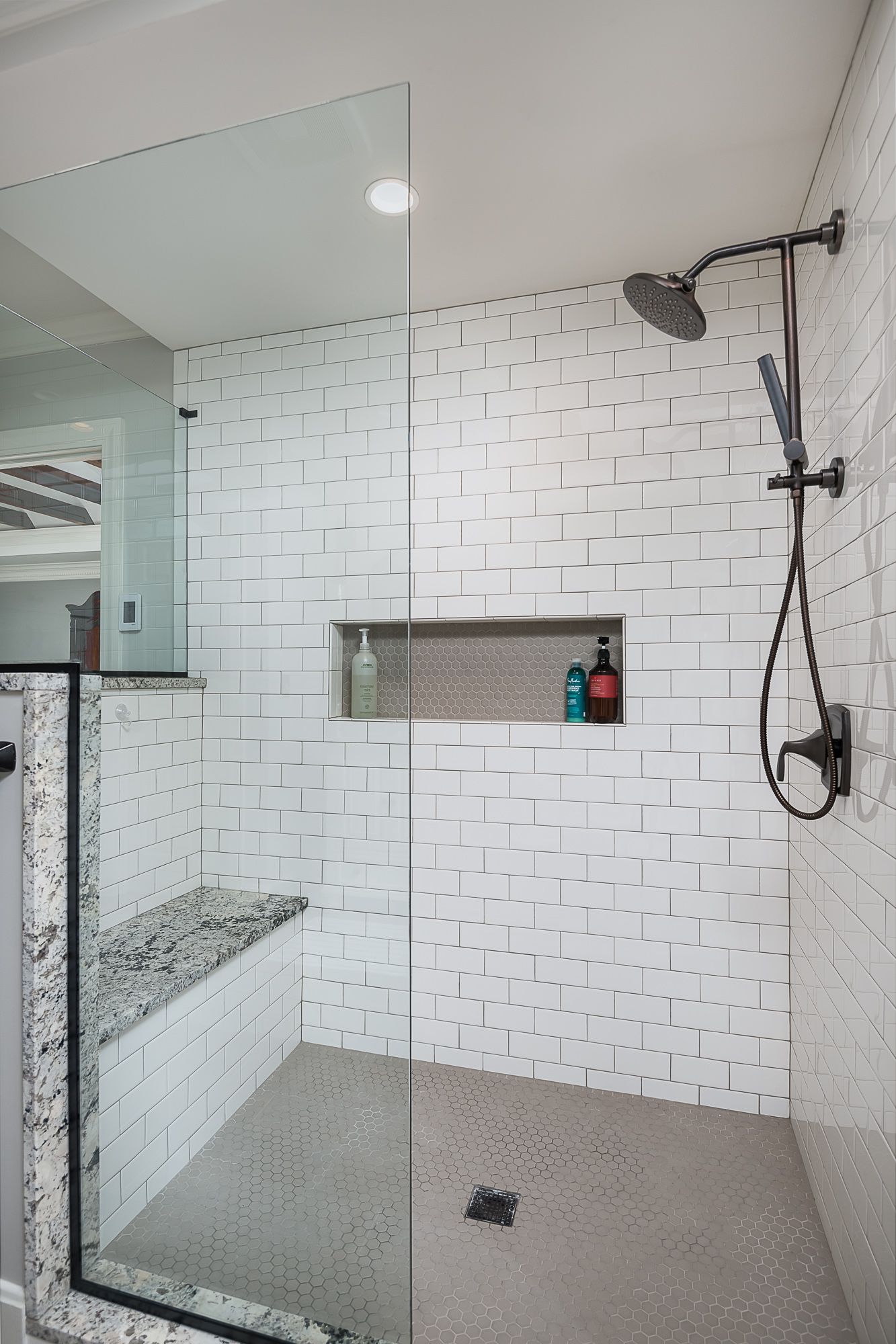 A walk in shower with white tiles and a glass door.