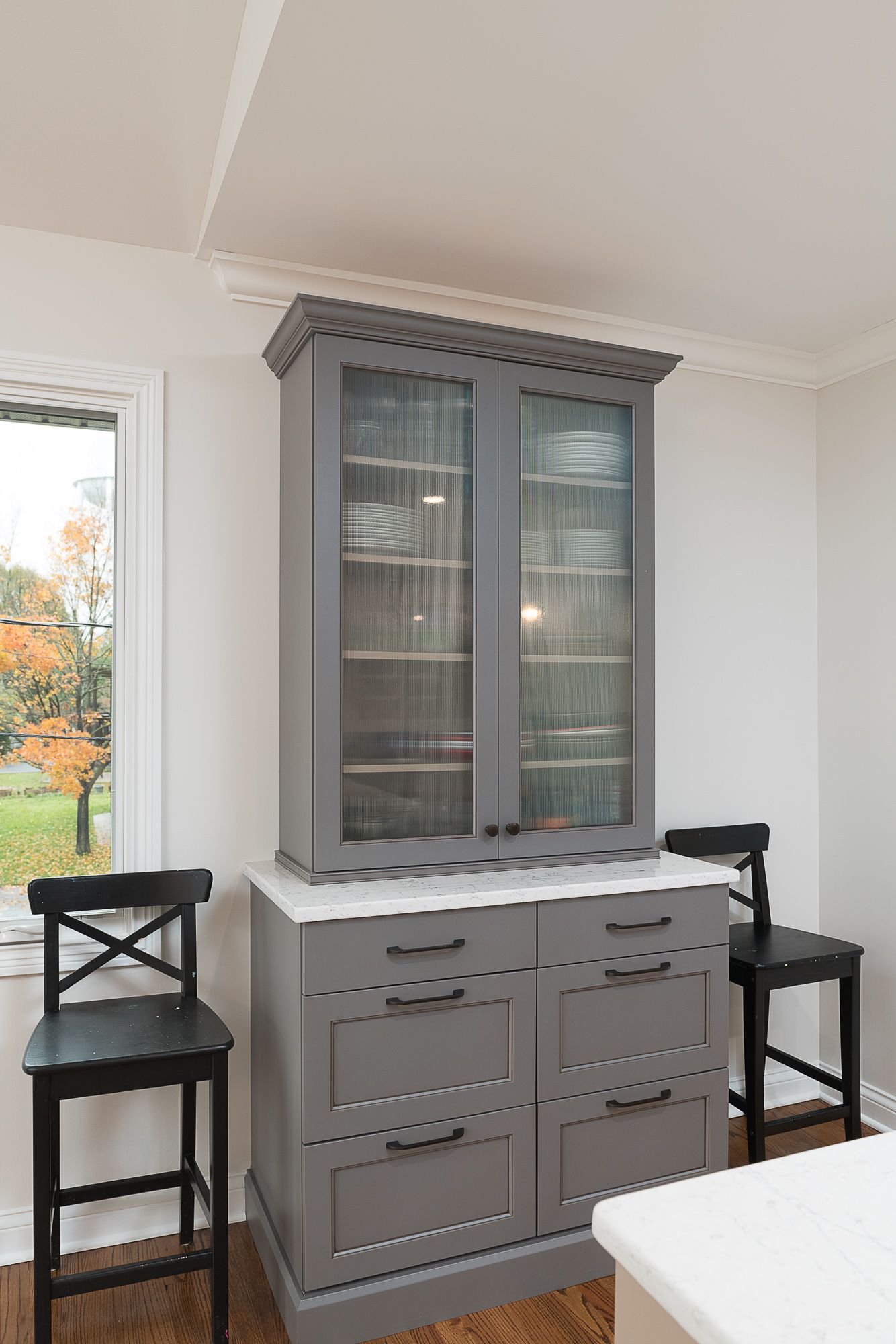 A gray cabinet with glass doors is in a kitchen next to a window.