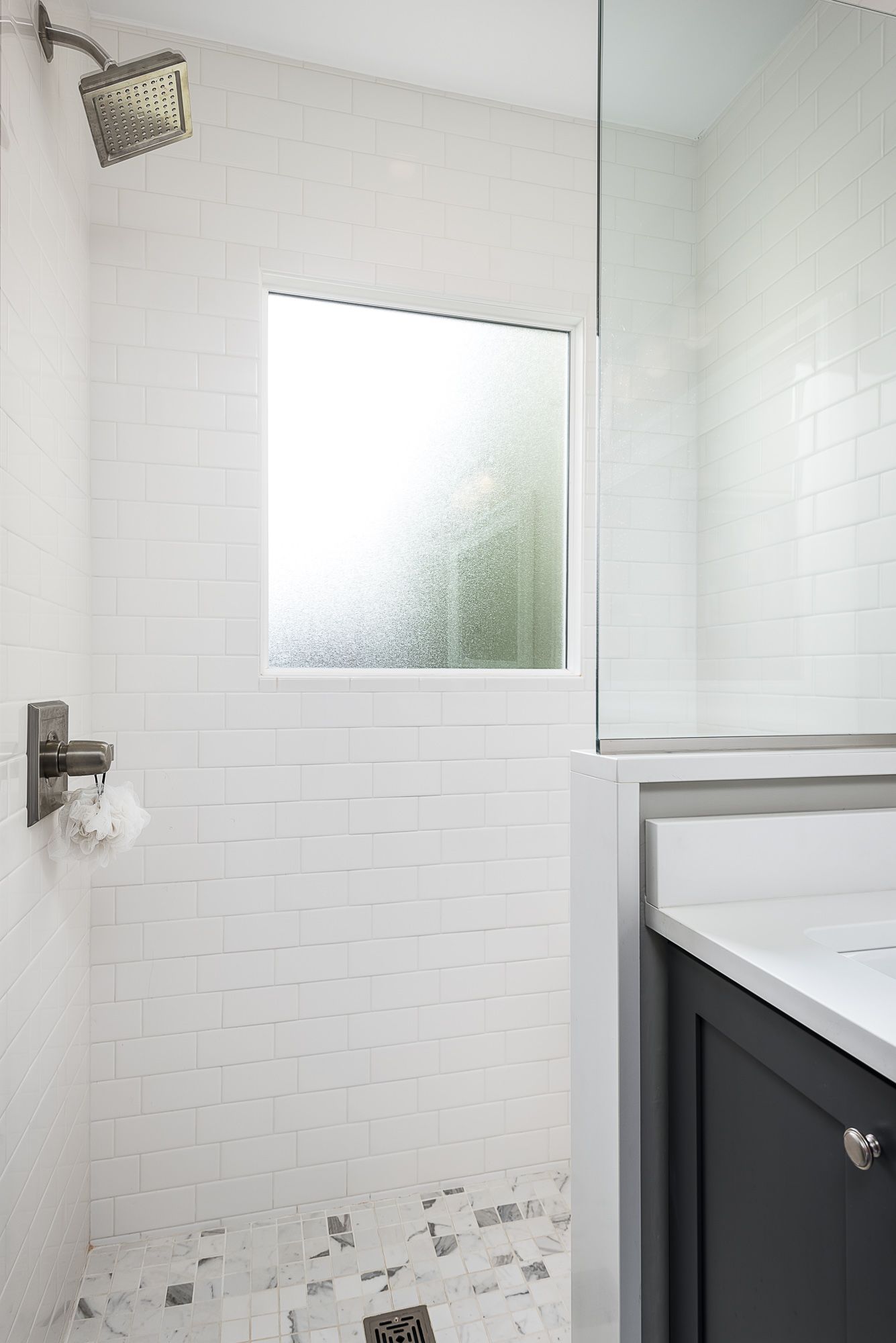 A bathroom with a walk in shower , sink , mirror and window.