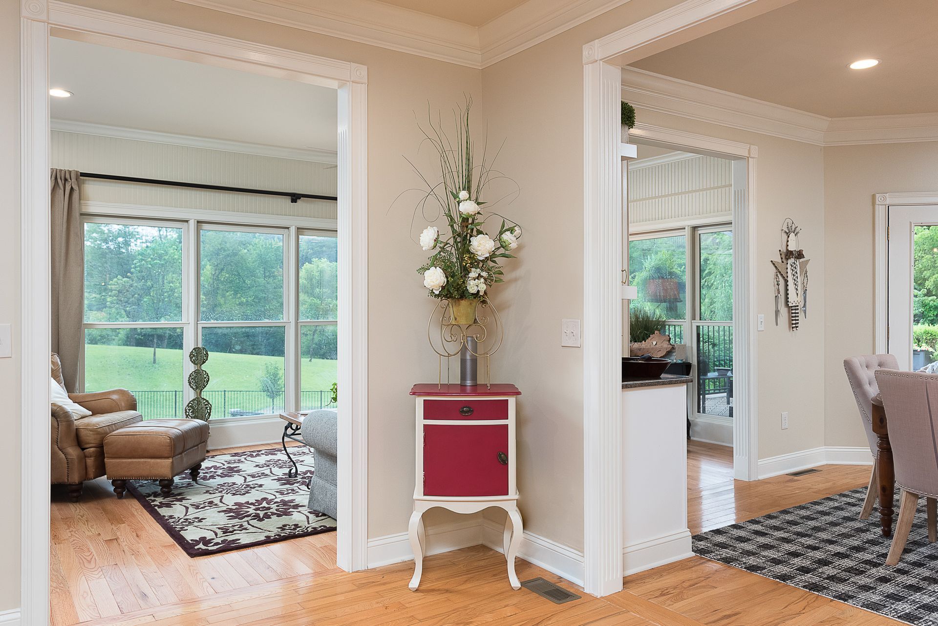 A living room with hardwood floors and a red table with a vase of flowers on it.