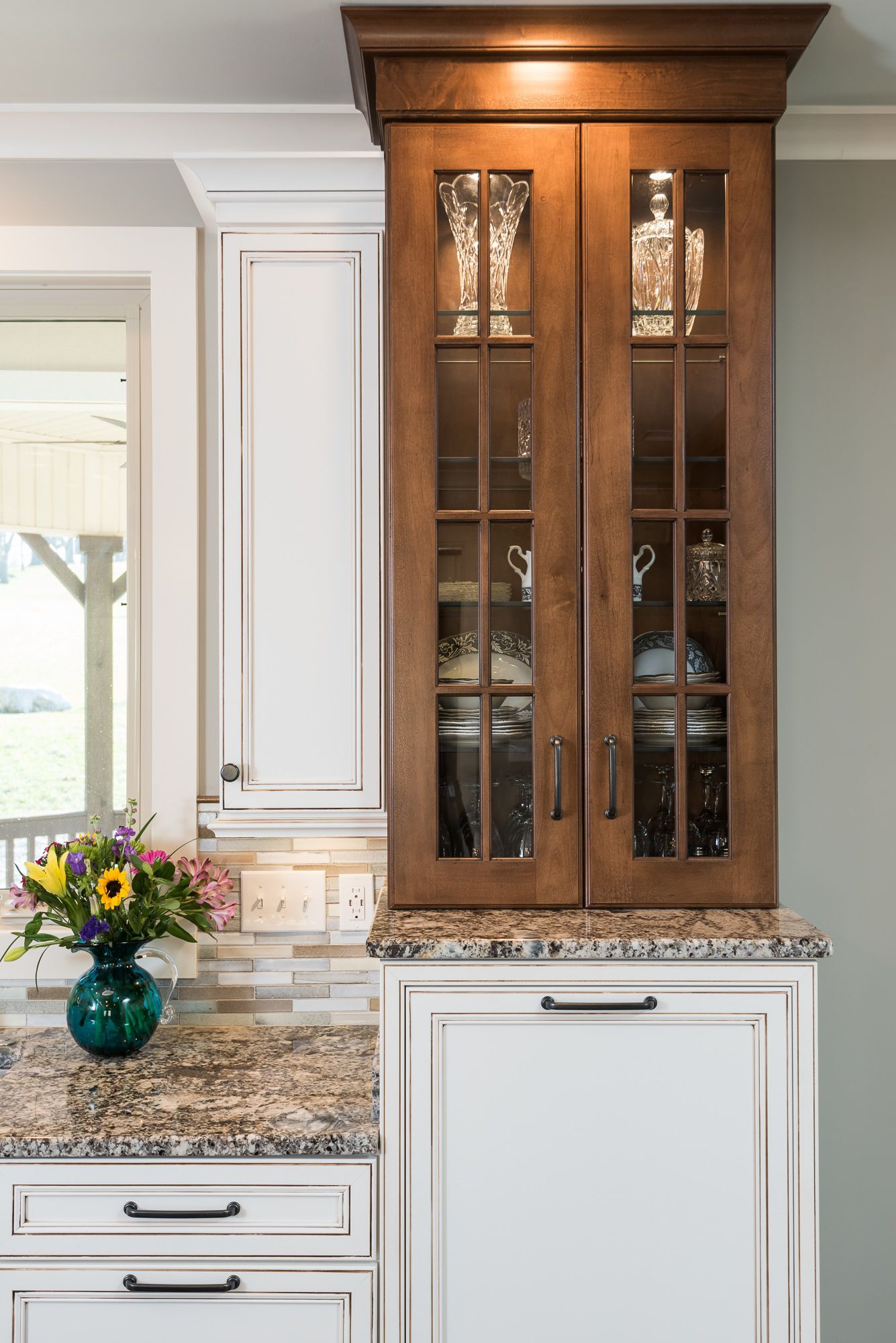 A kitchen with white cabinets and a glass cabinet with a vase of flowers on the counter.