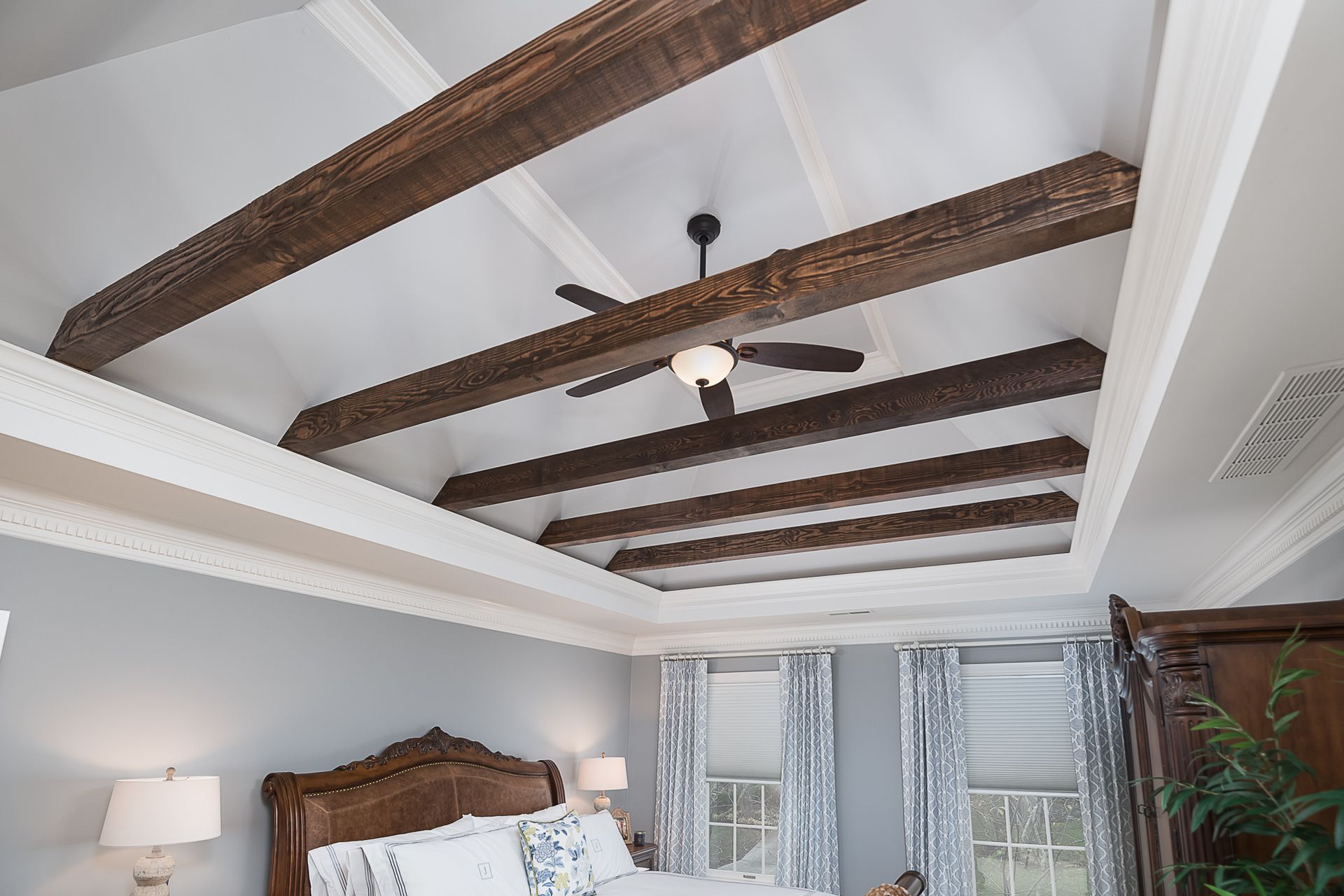 A bedroom with a ceiling fan and wooden beams on the ceiling.