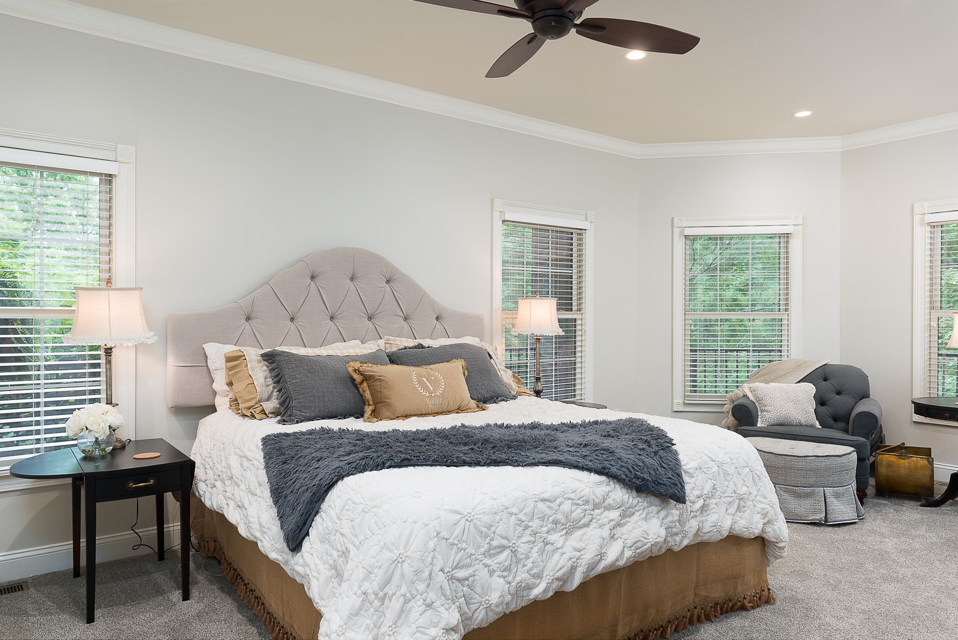 A bedroom with a large bed , a ceiling fan , and two windows.
