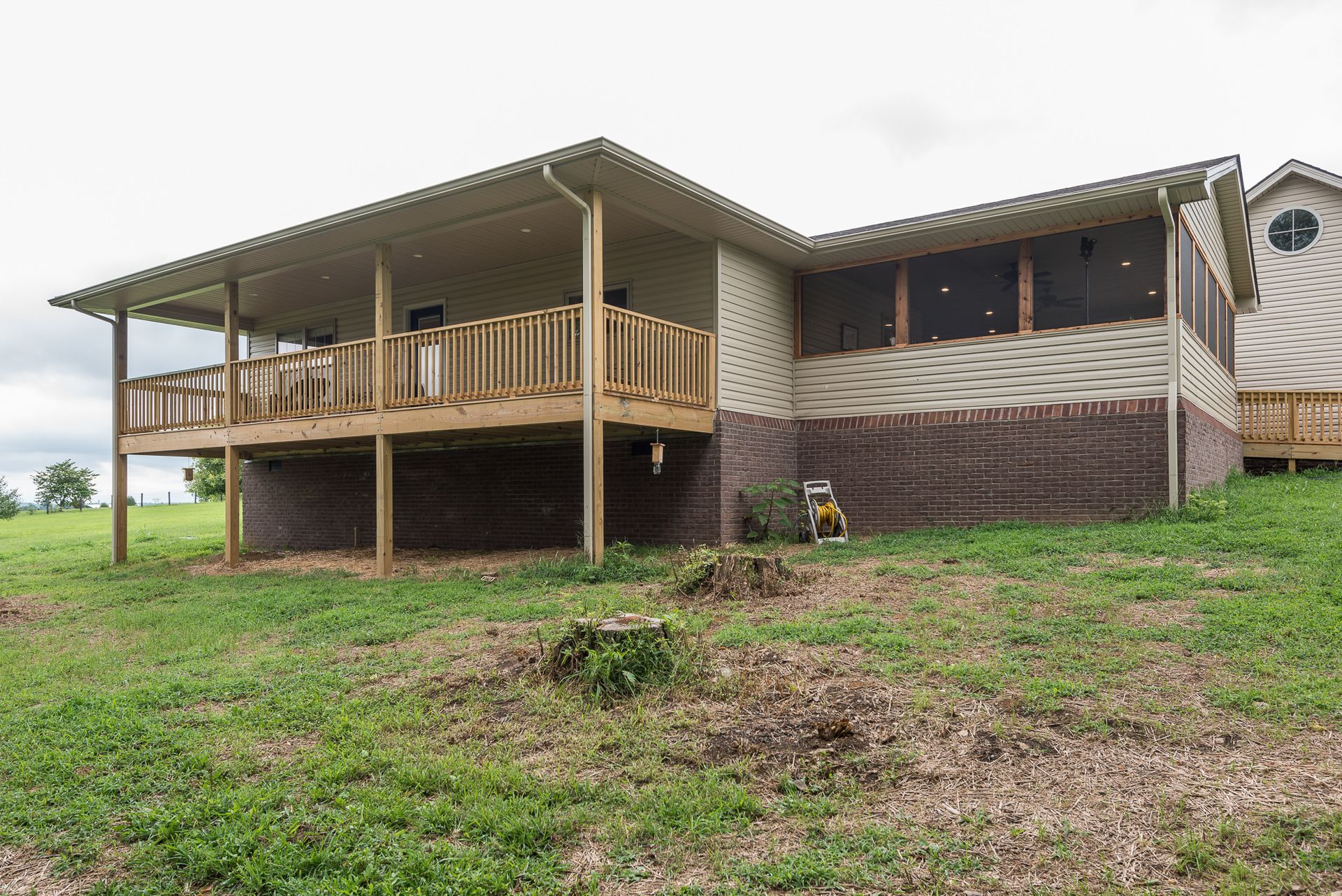 A large house with a large deck is sitting on top of a grassy hill.