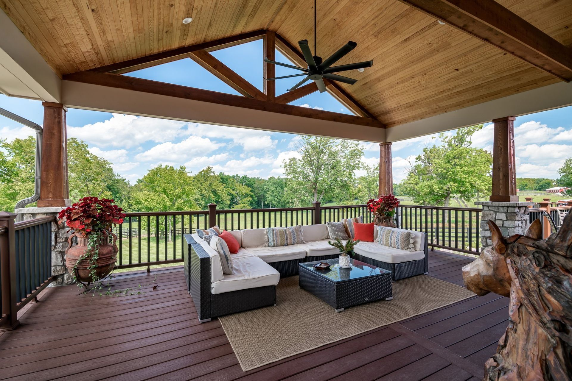 A large deck with a couch , table , and ceiling fan.