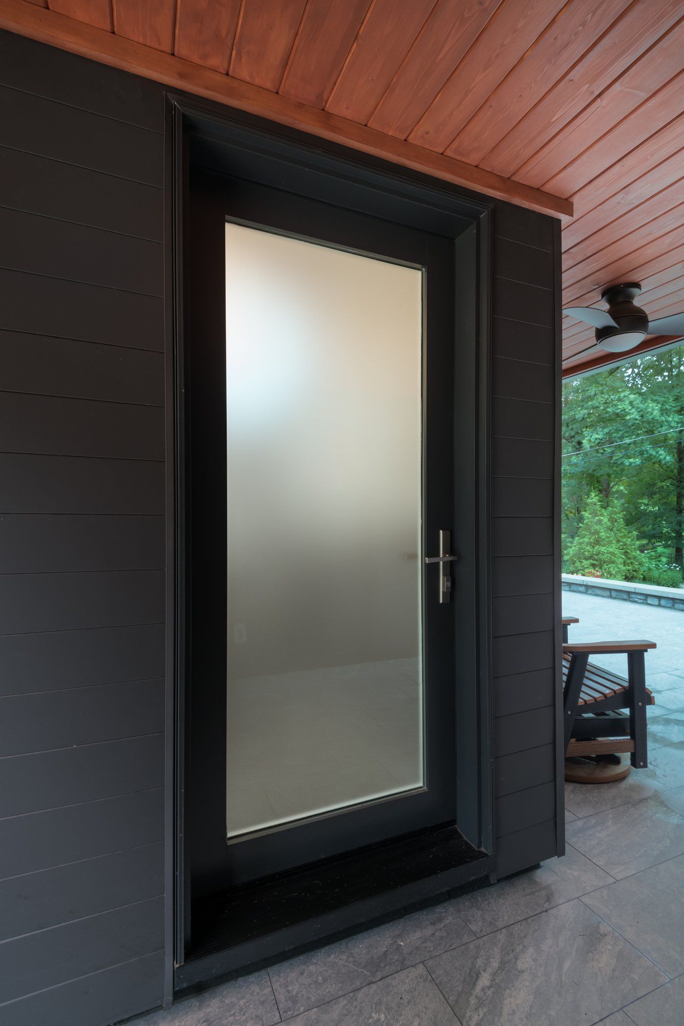 A black door with a frosted glass window is on a black wall.