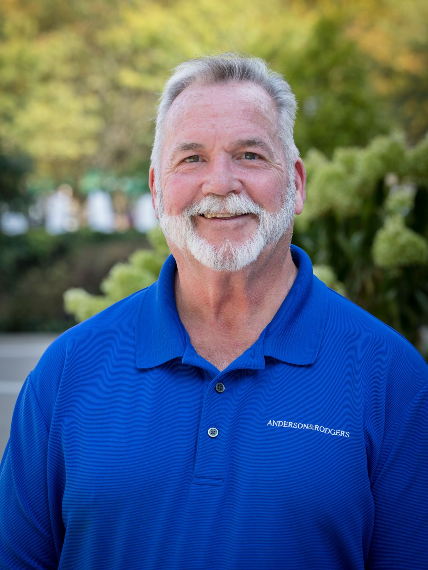 A man with a beard is wearing a striped shirt and smiling.