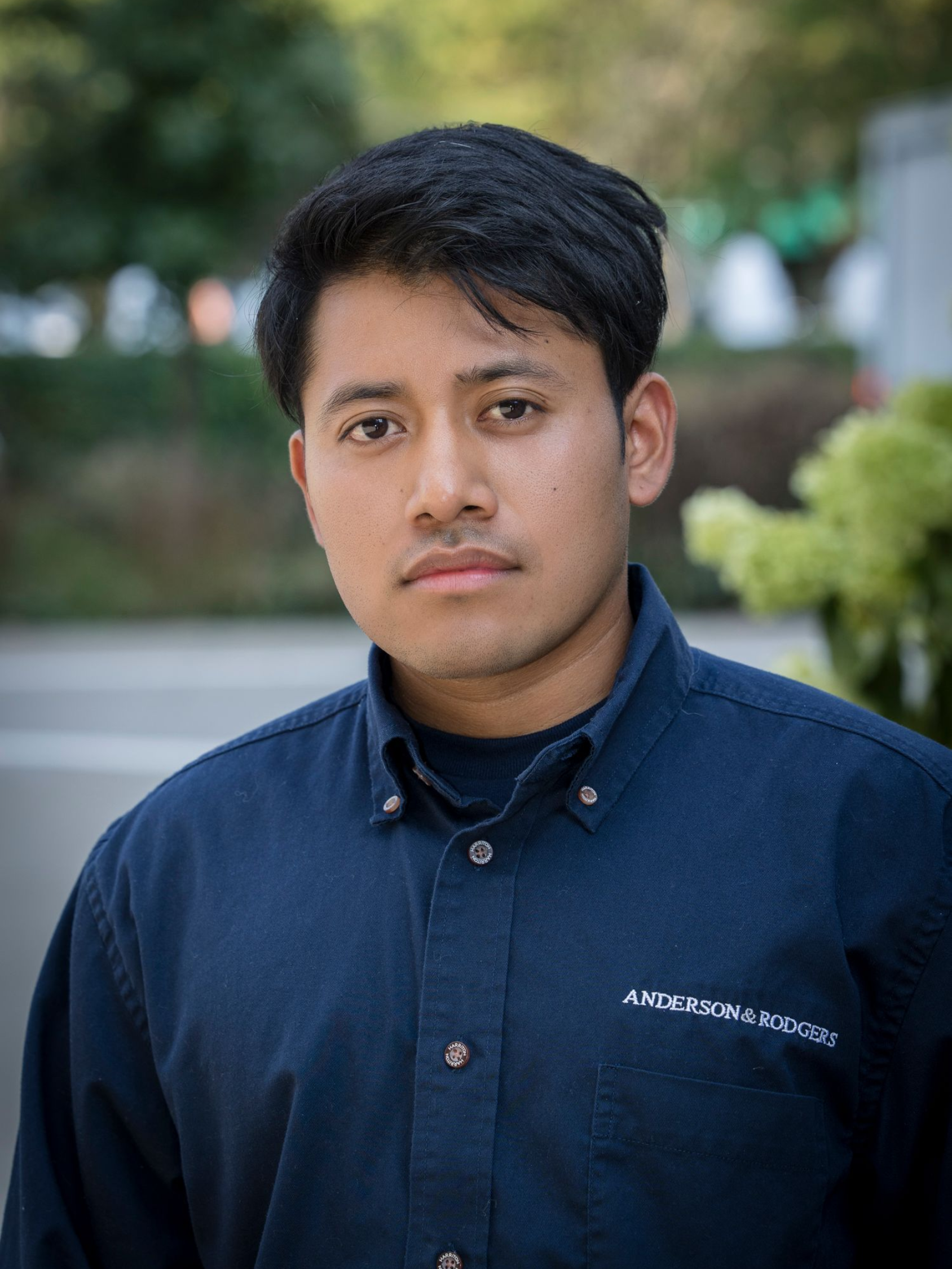 A young man wearing a blue jacket and earrings is standing in front of a building.