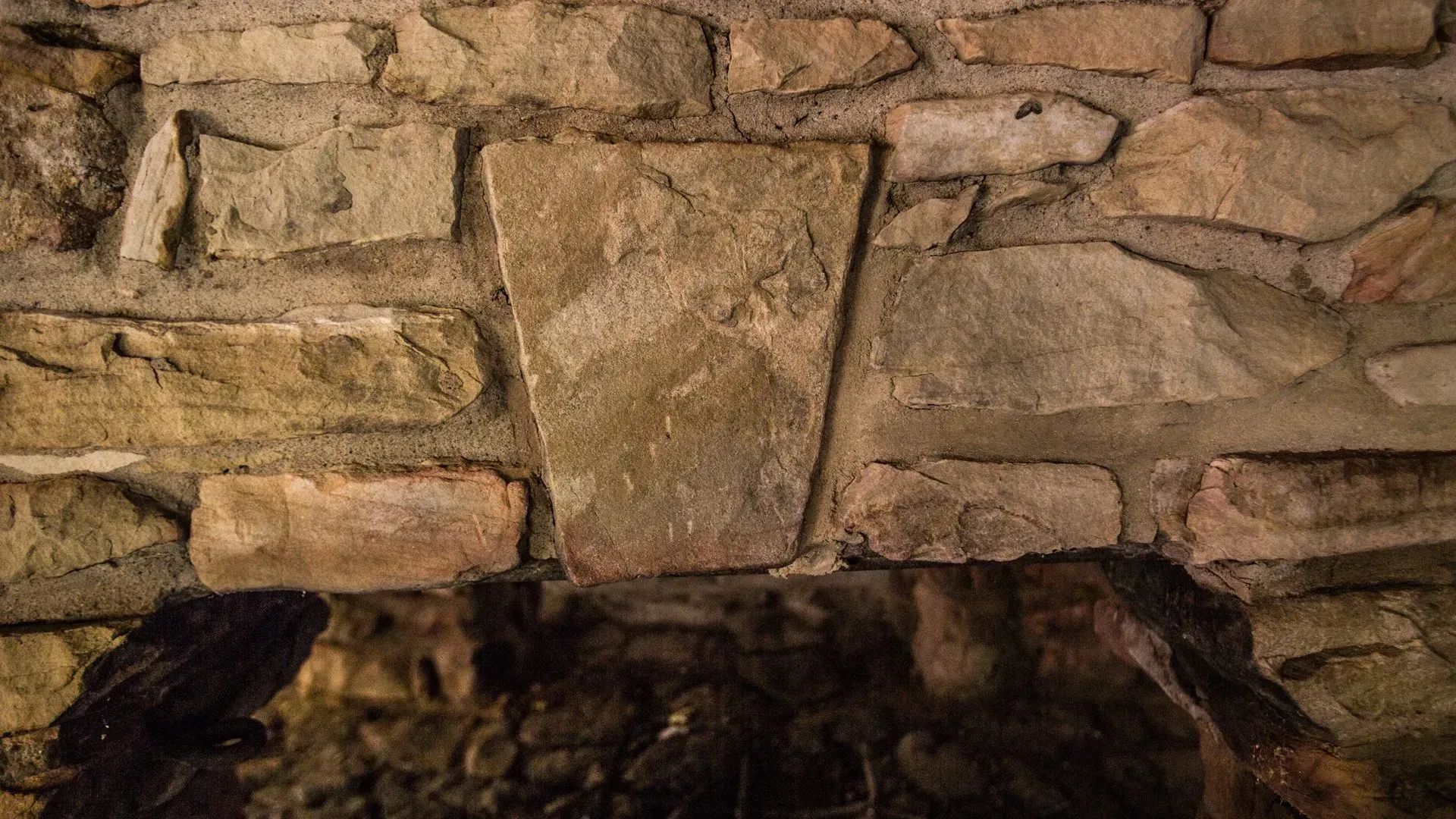 A close up of a stone wall with a fireplace in the background.