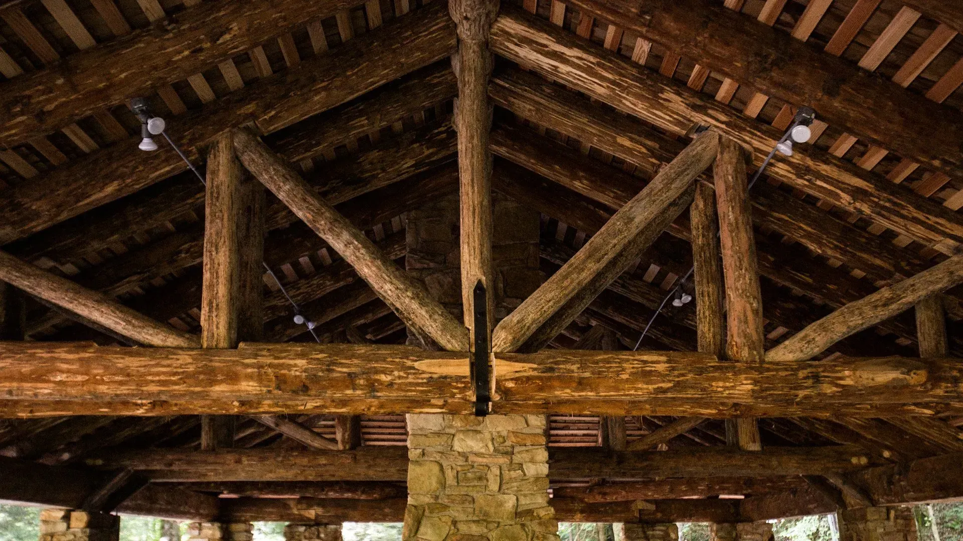 The ceiling of a building made of wooden beams and a stone chimney.