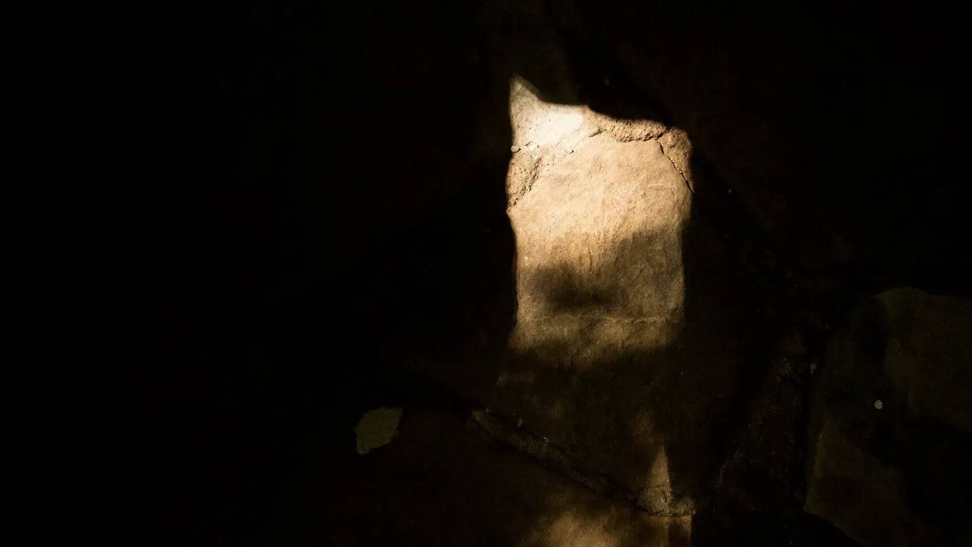 A person is standing in a dark room with a light coming out of the doorway.
