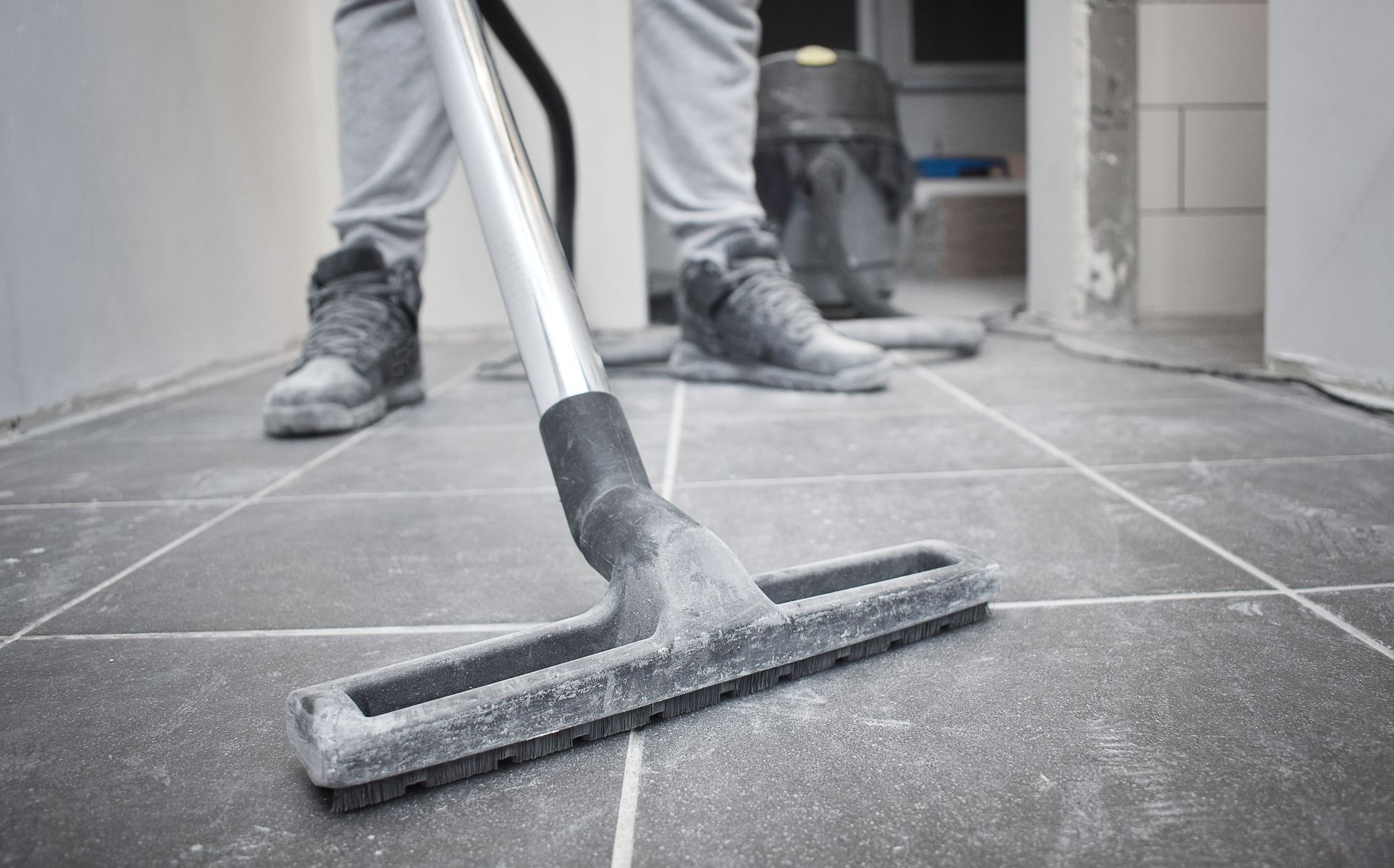 Person mopping a gray tiled floor with a white mop in a hallway under construction