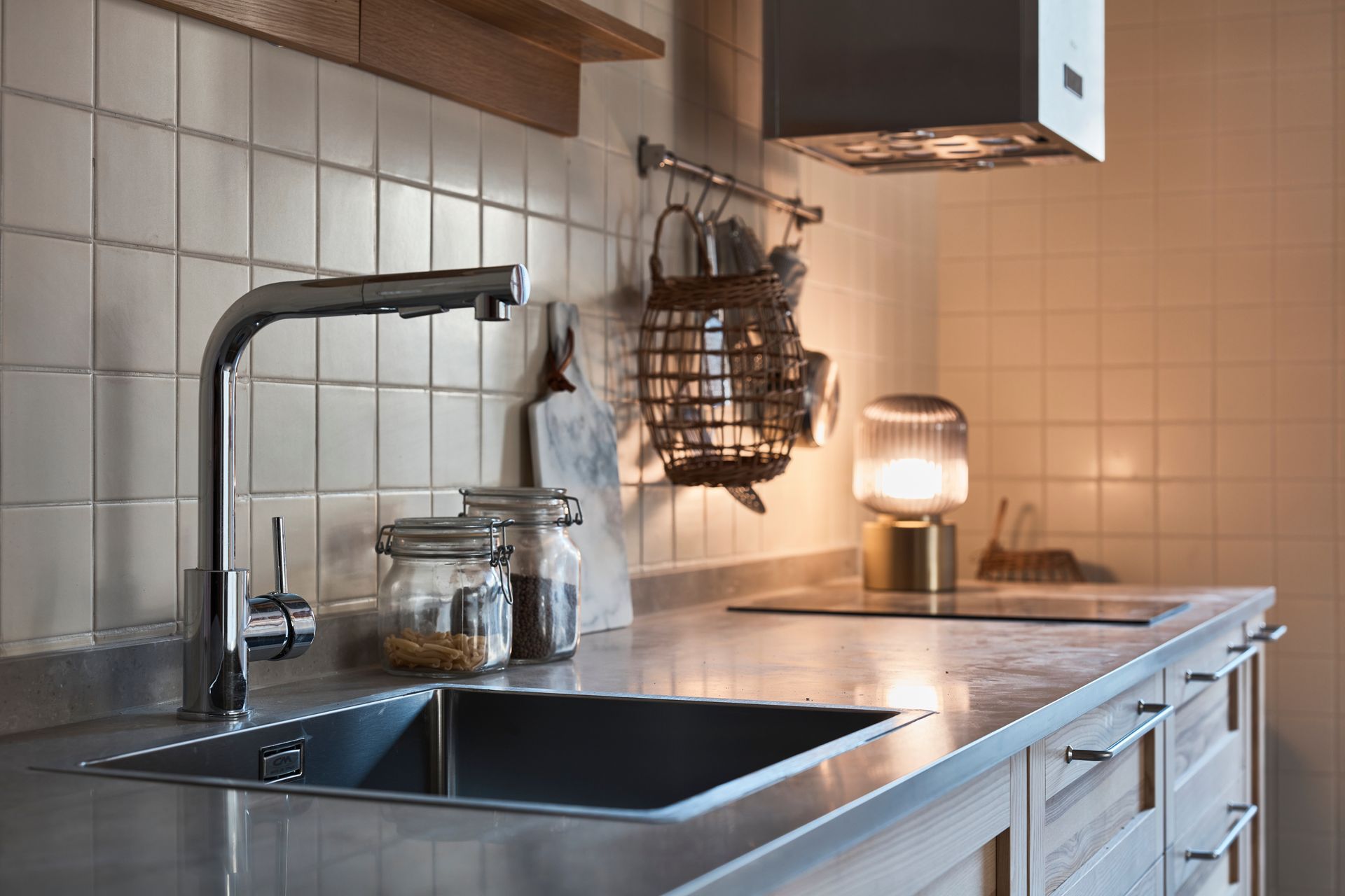 Modern kitchen with black sink, light wood cabinets, tiled backsplash, and warm countertop lamp