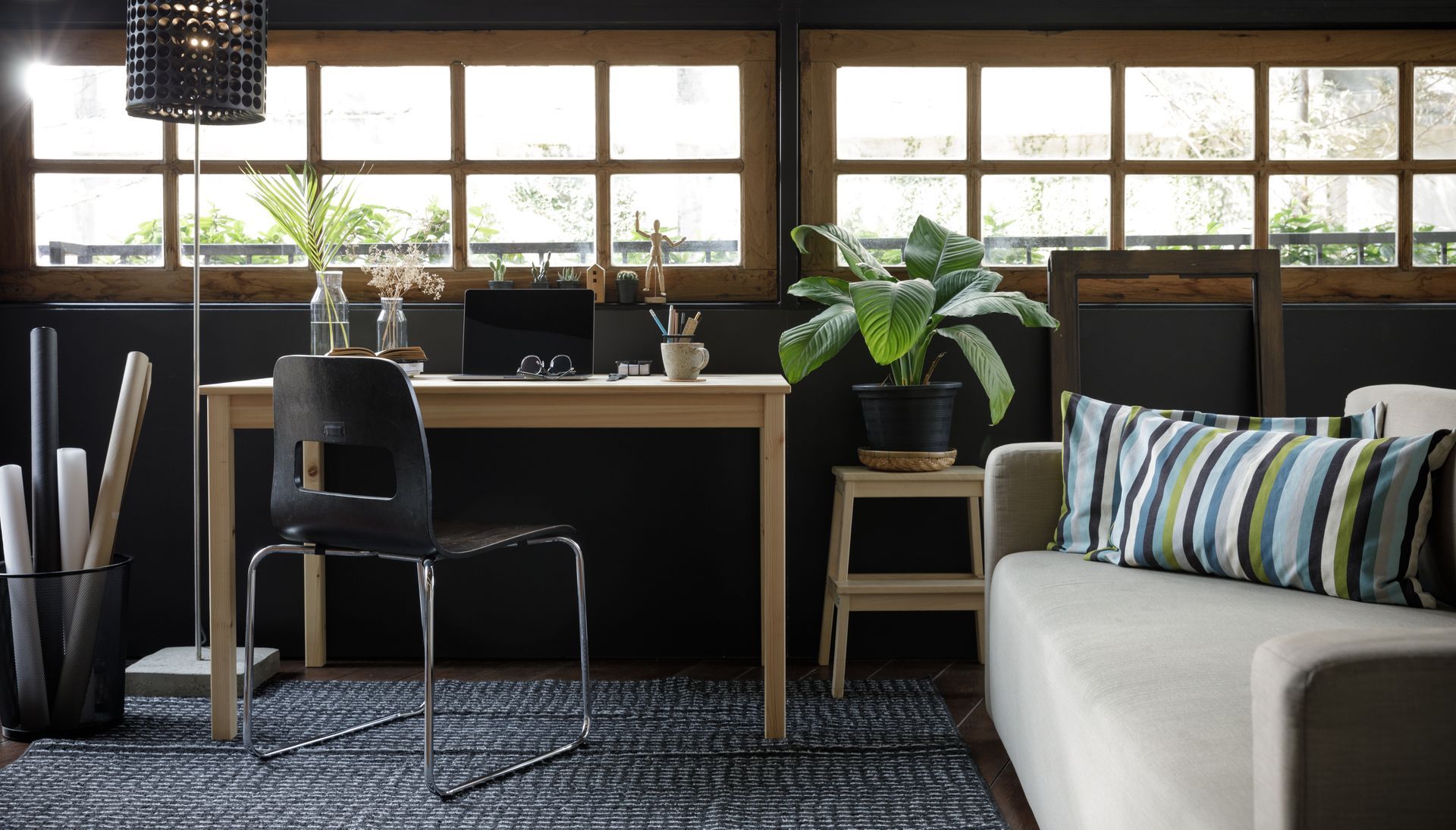 Modern home office with desk, chair, plants, and a sofa by large windows