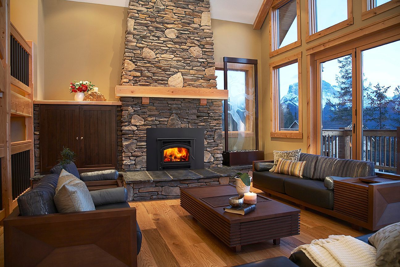 Cozy living room with stone fireplace, leather sofas, and large windows overlooking dusk outside